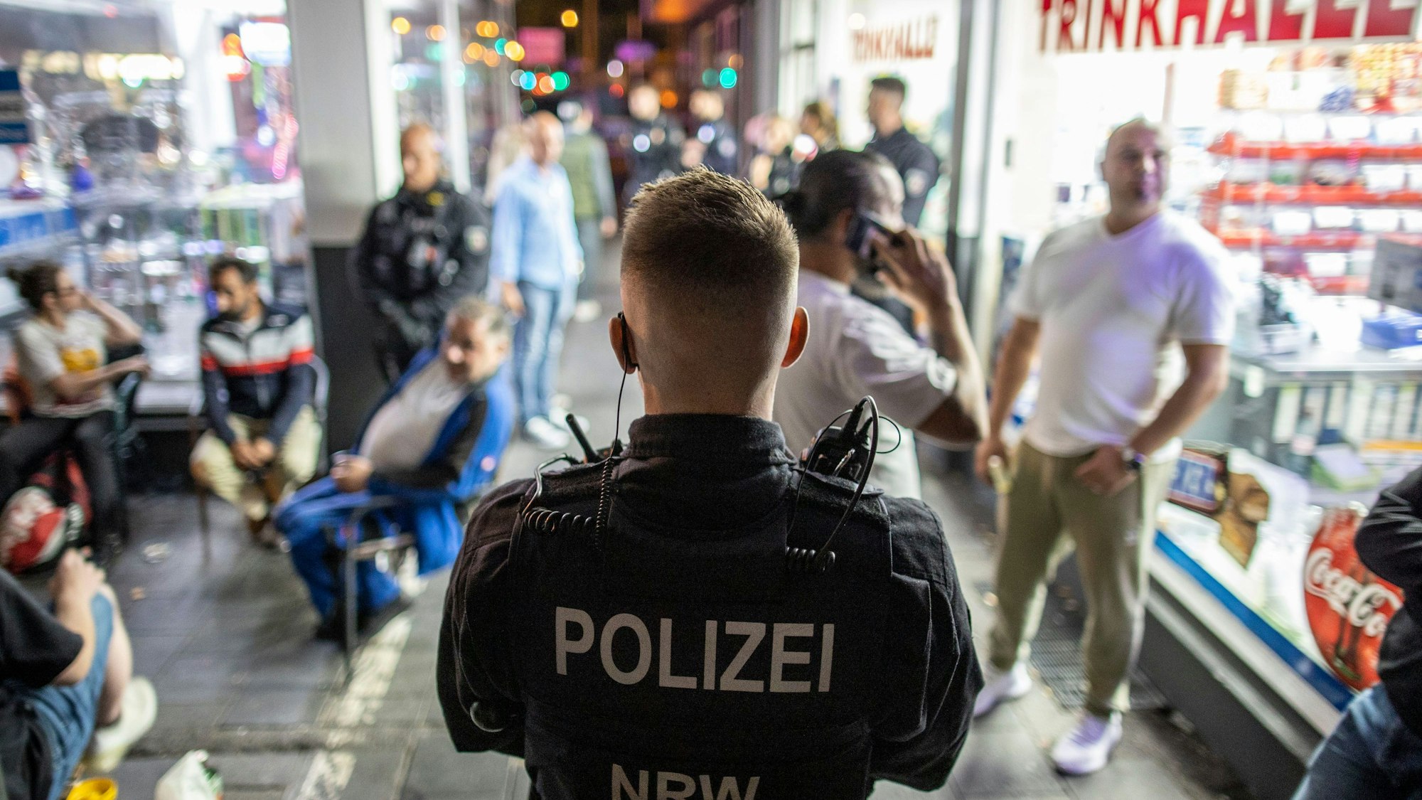 26.08.2022, Nordrhein-Westfalen, Duisburg: Ein Polizist steht im Zuge einer Razzia im Duisburger Norden am Freitagabend vor einer Trinkhalle und überwacht die Gäste des Lokals.