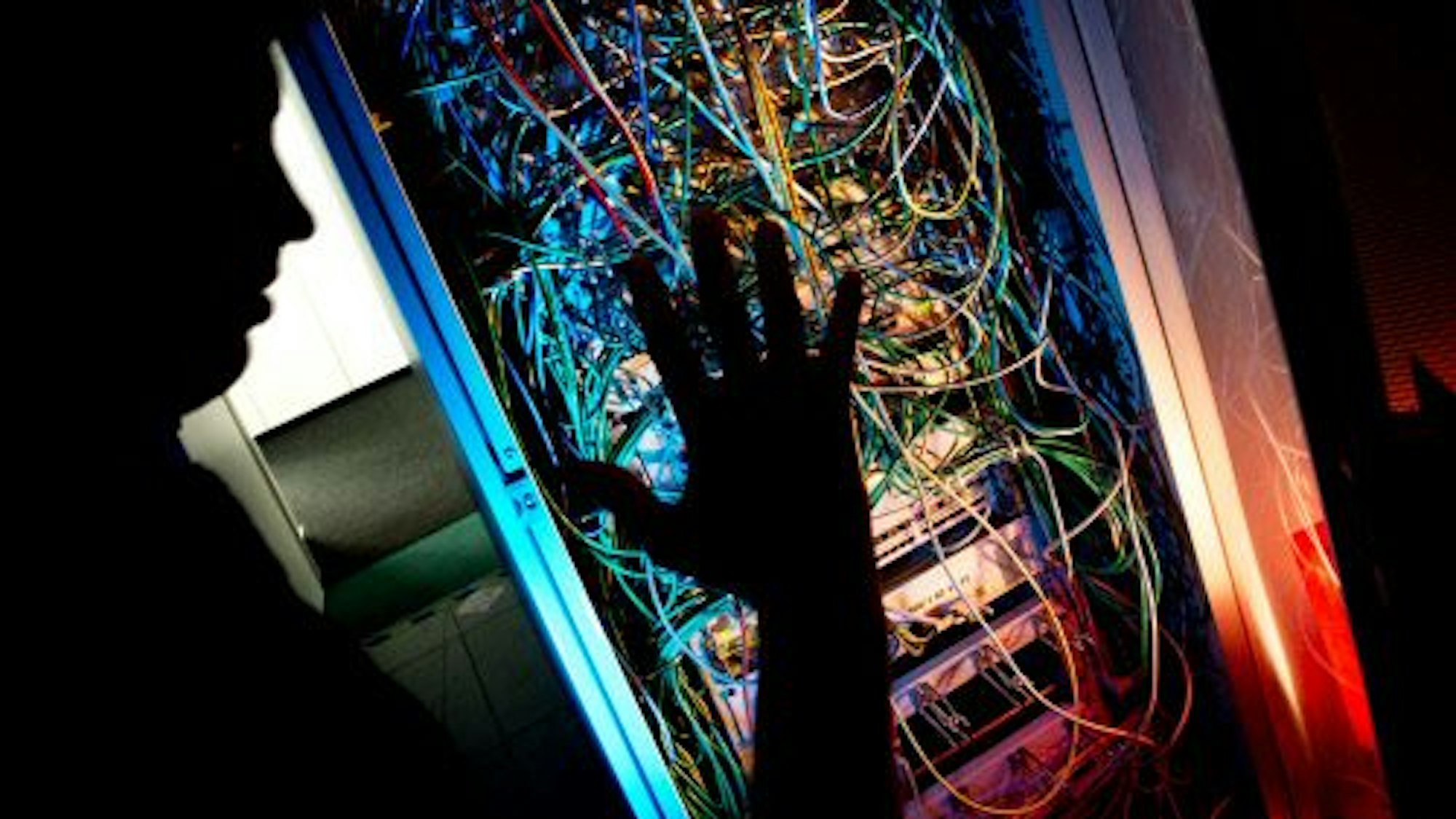 Ein Mann steht an einem Serverschrank aus dem ganz viele Kabel raushängen. - Symbolfoto zum Thema Kinderpornografie