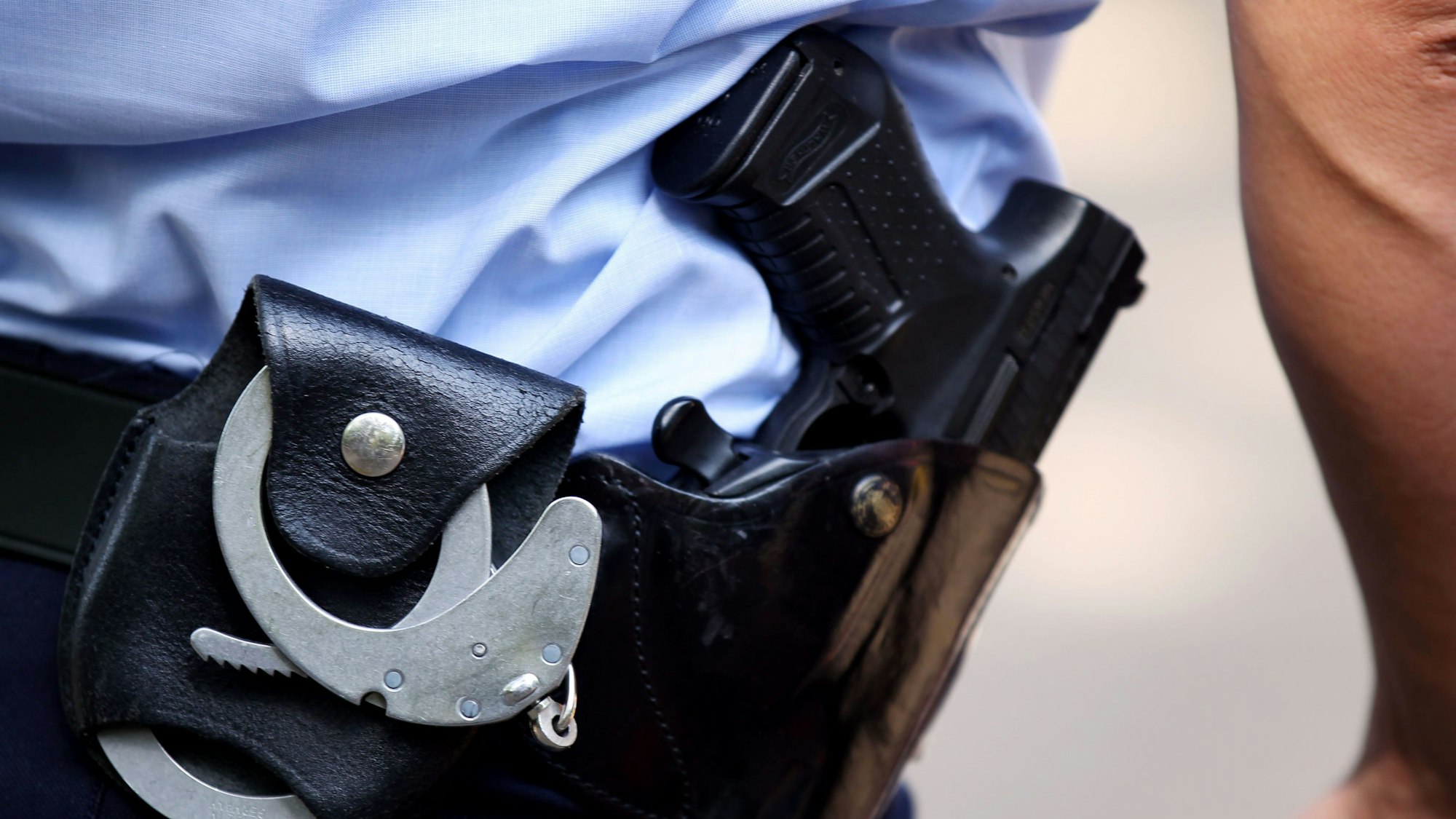 Das Symbolfoto (Detailaufnahme) zeigt Dienstwaffe und Handfesseln eines Polizeibeamten.