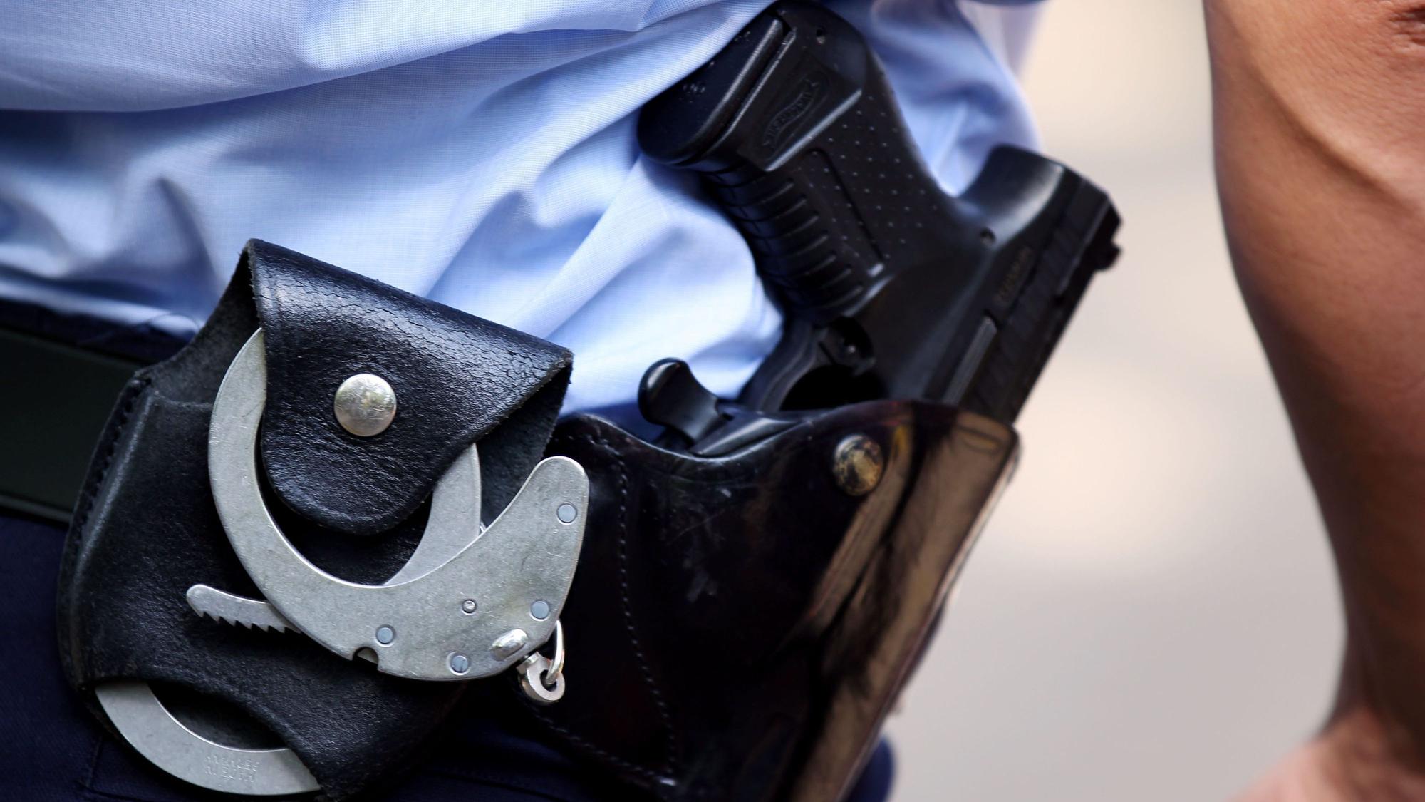 Ein Polizist mit Handschellen und Pistole am Gürtel steht in Köln auf einem Schulhof.