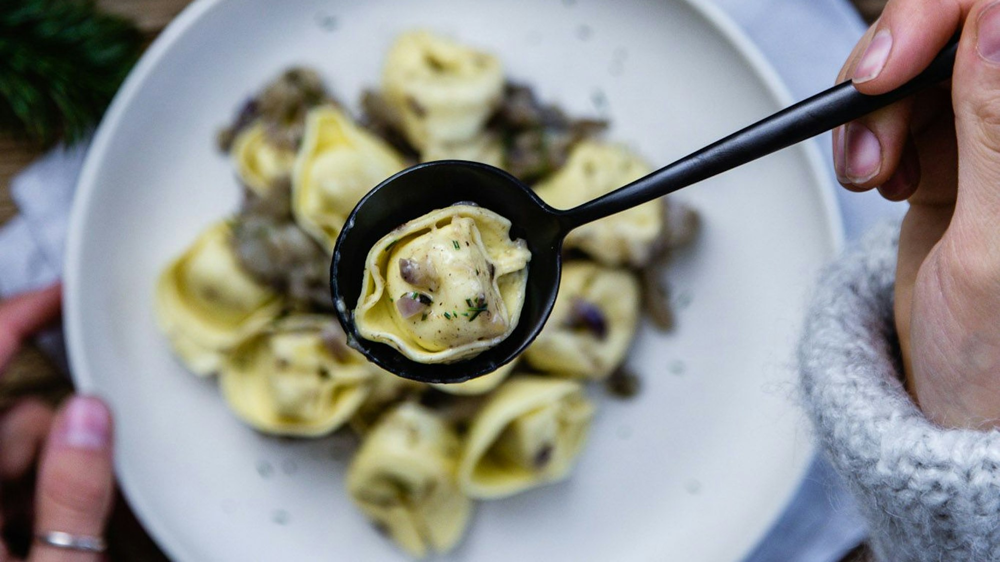 Waldige Tortellini di bosco liegen auf einem Teller und werden mit einem Löffel gegessen.