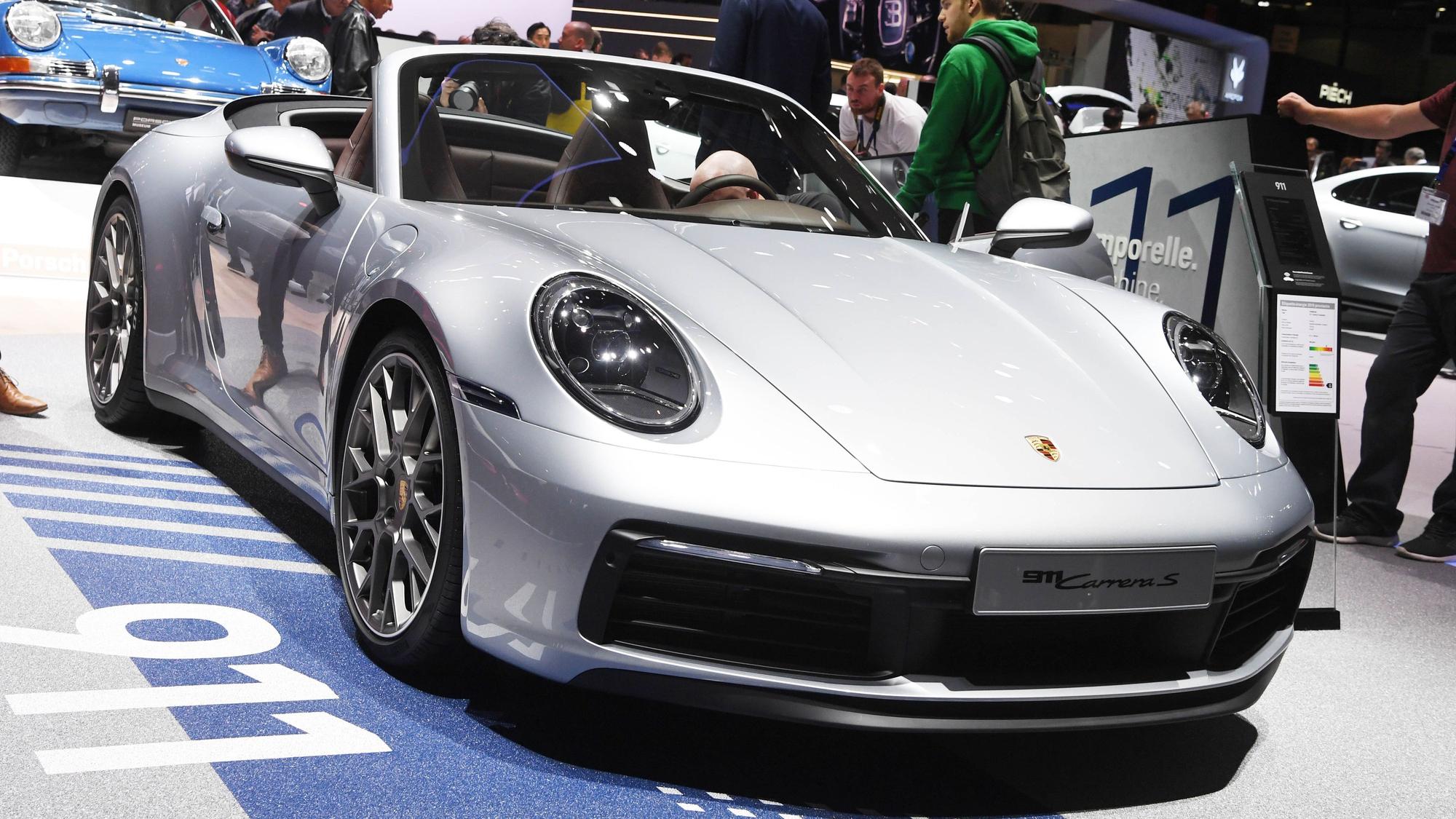Auf dem Genfer Autosalon wird ein Porsche 911 Cabriolet präsentiert. Es it ein silberner Sportwagen mit dem Porsche-Logo.