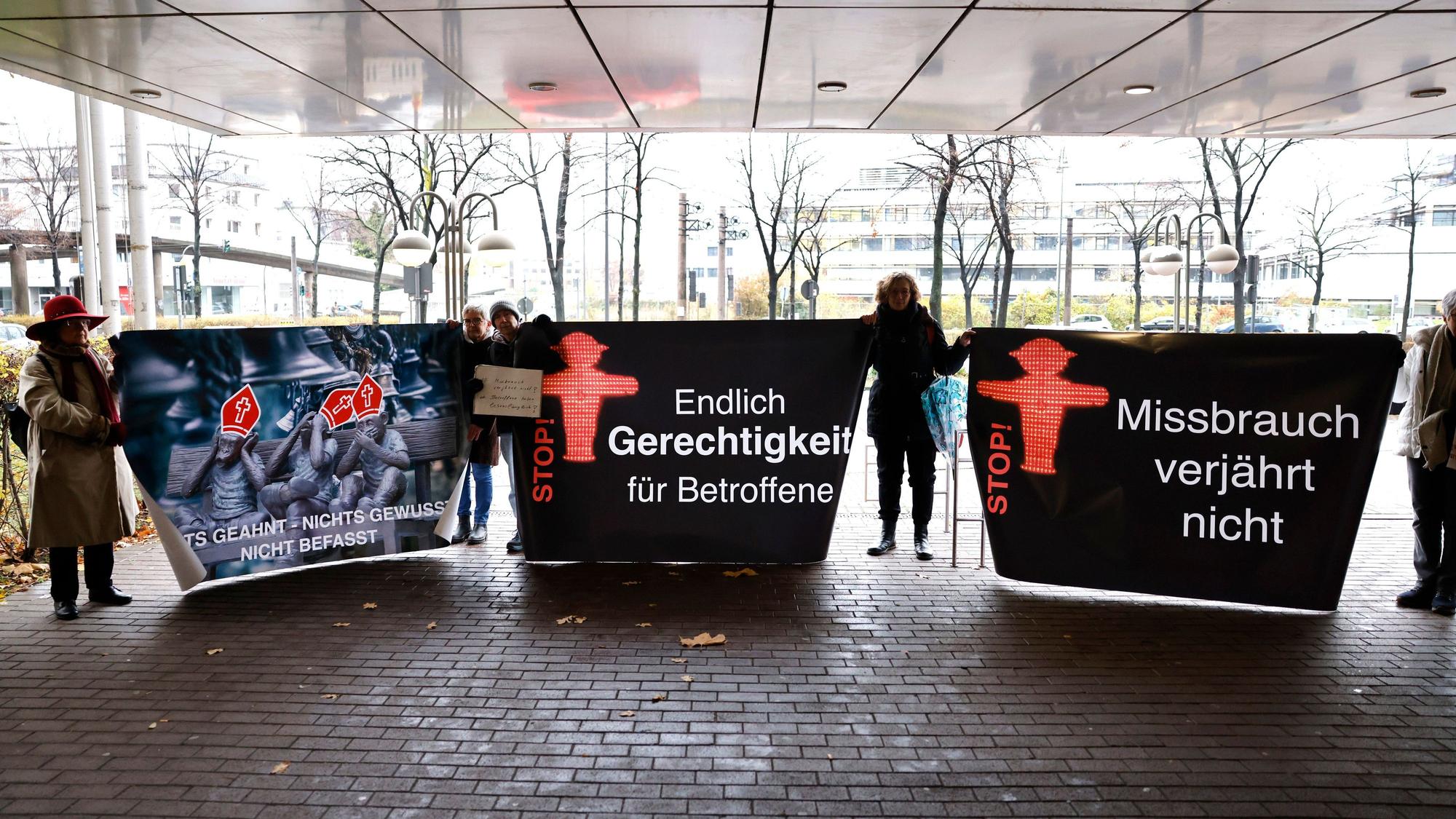 06.12.2022, Nordrhein-Westfalen, Köln: Unterstützer von Kläger Georg Menne stehen vor dem Landgericht Köln und halten Plakate mit der Aufschrift: "Missbrauch verjährt nicht" und "Endlich Gerechtigkeit für Betroffene" hoch.