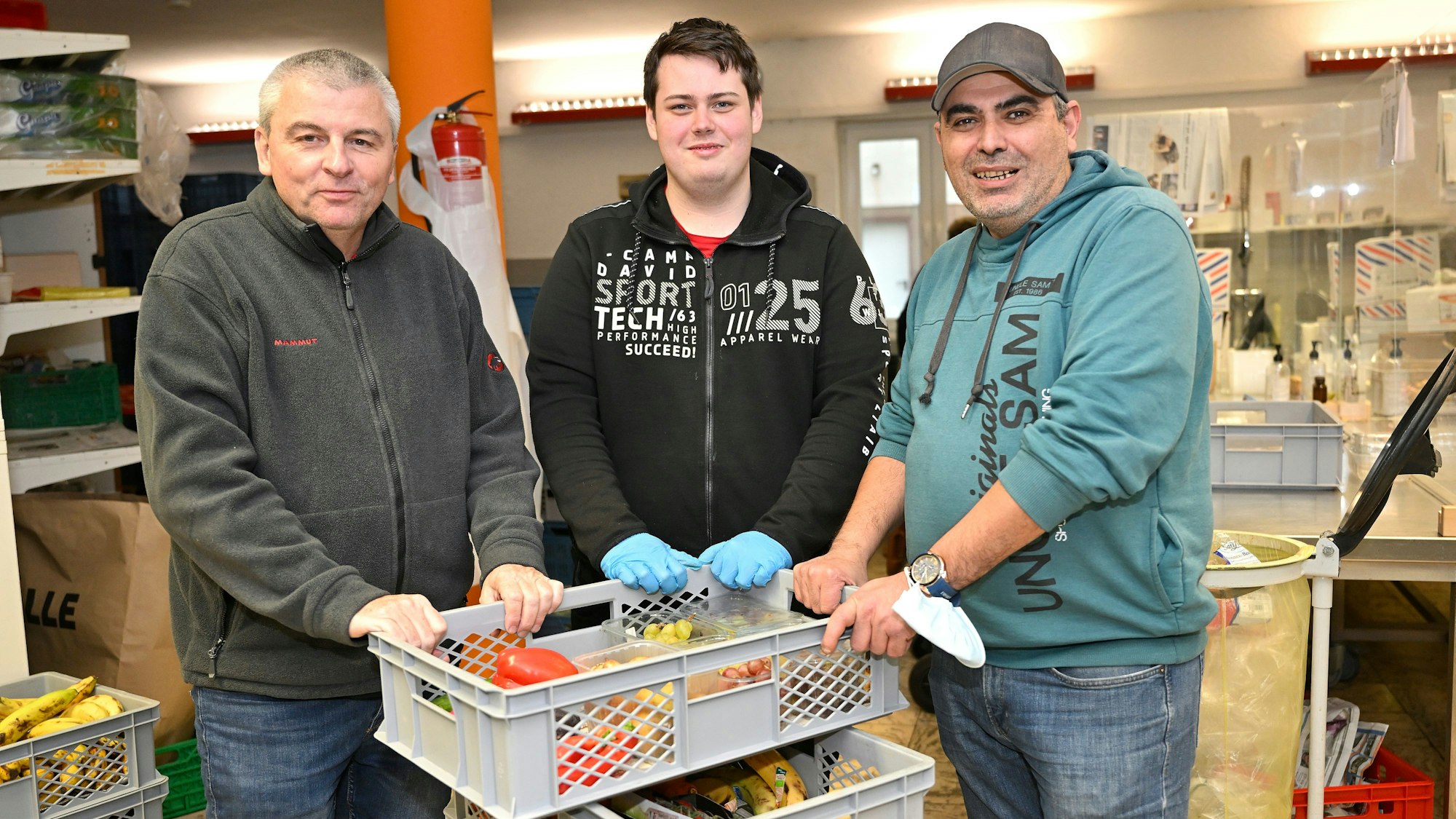 Markus Kerkhoff, Jan Drouve, Tarik Areslan stehen vor Kisten mit Lebensmitteln.