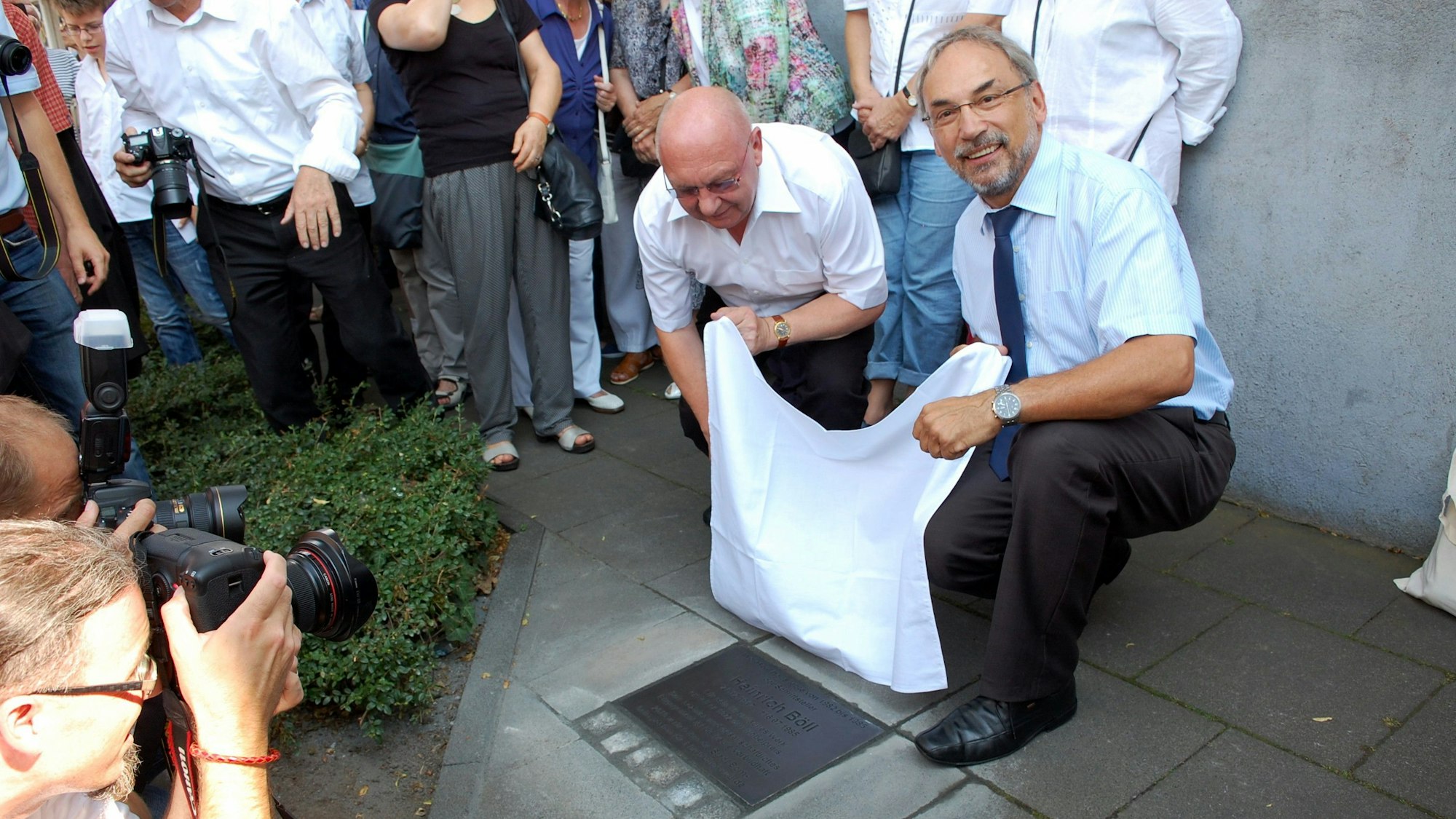 Der damalige Bornheimer Bürgermeister Wolfgang Henseler (rechts) und Mertens Ortsvorsther Hans Gerd Feldenkirchen knien im Juli 2015 vor Bölls Wohnhaus in Merten und enthüllen eine Gedenkplatte.