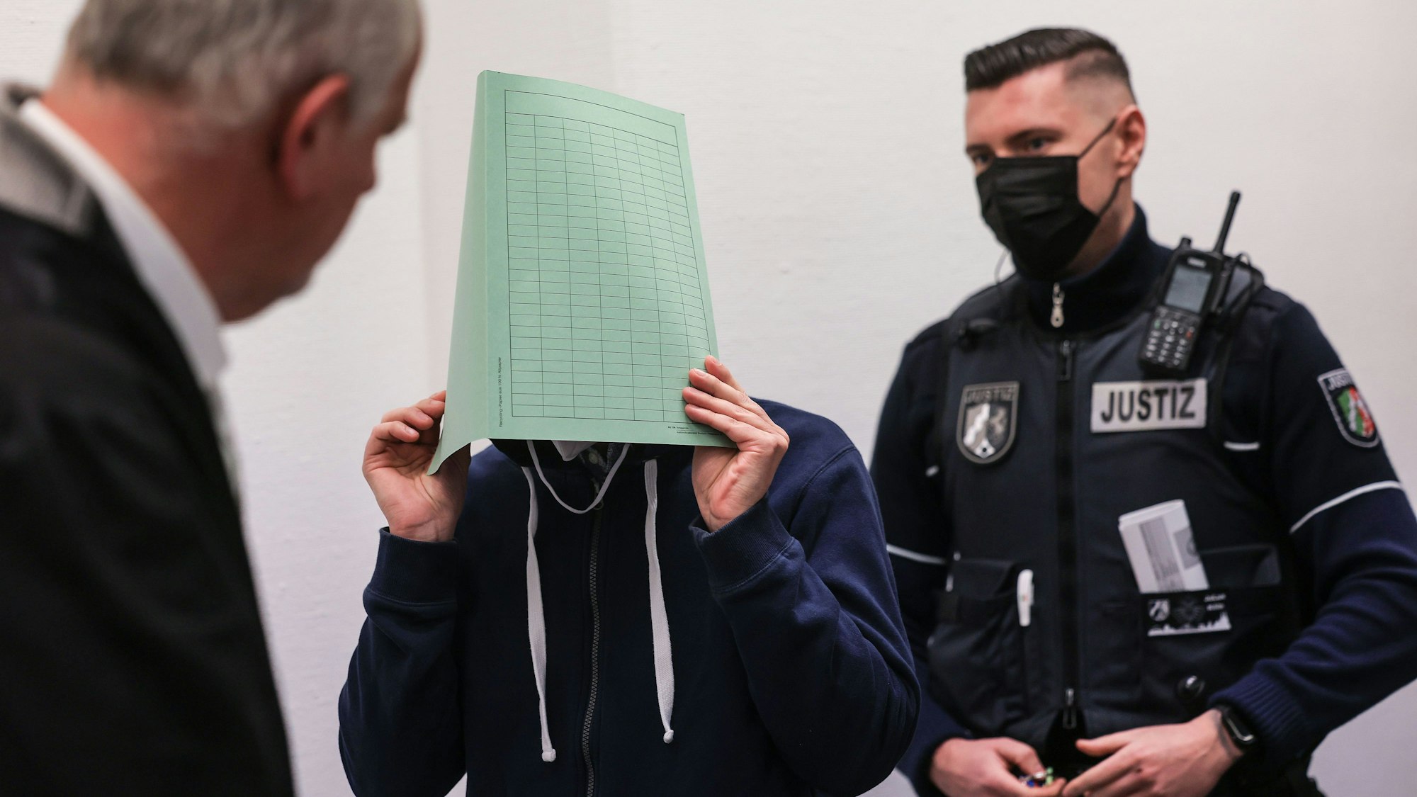 Der Angeklagte im Missbrauchskomplex Wermelskirchen hält sich beim Betreten des Gerichtssaals neben seinem Rechtsanwalt Christian Lange eine Mappe vor das Gesicht. Der Mann soll sich im Internet als Babysitter angeboten und so Kontakt zu den Familien der Opfer bekommen haben.