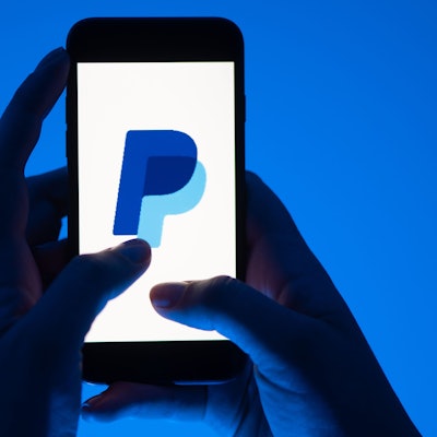 Eine Frau hält ein Smartphone mit dem Logo des Bezahldienst Paypal in der Hand.