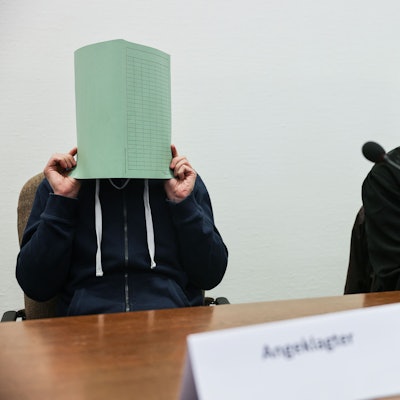 Der Angeklagte (l) im Missbrauchskomplex Wermelskirchen hält sich im Gerichtssaal neben seinem Rechtsanwalt Christian Lange (r) eine Mappe vor das Gesicht.