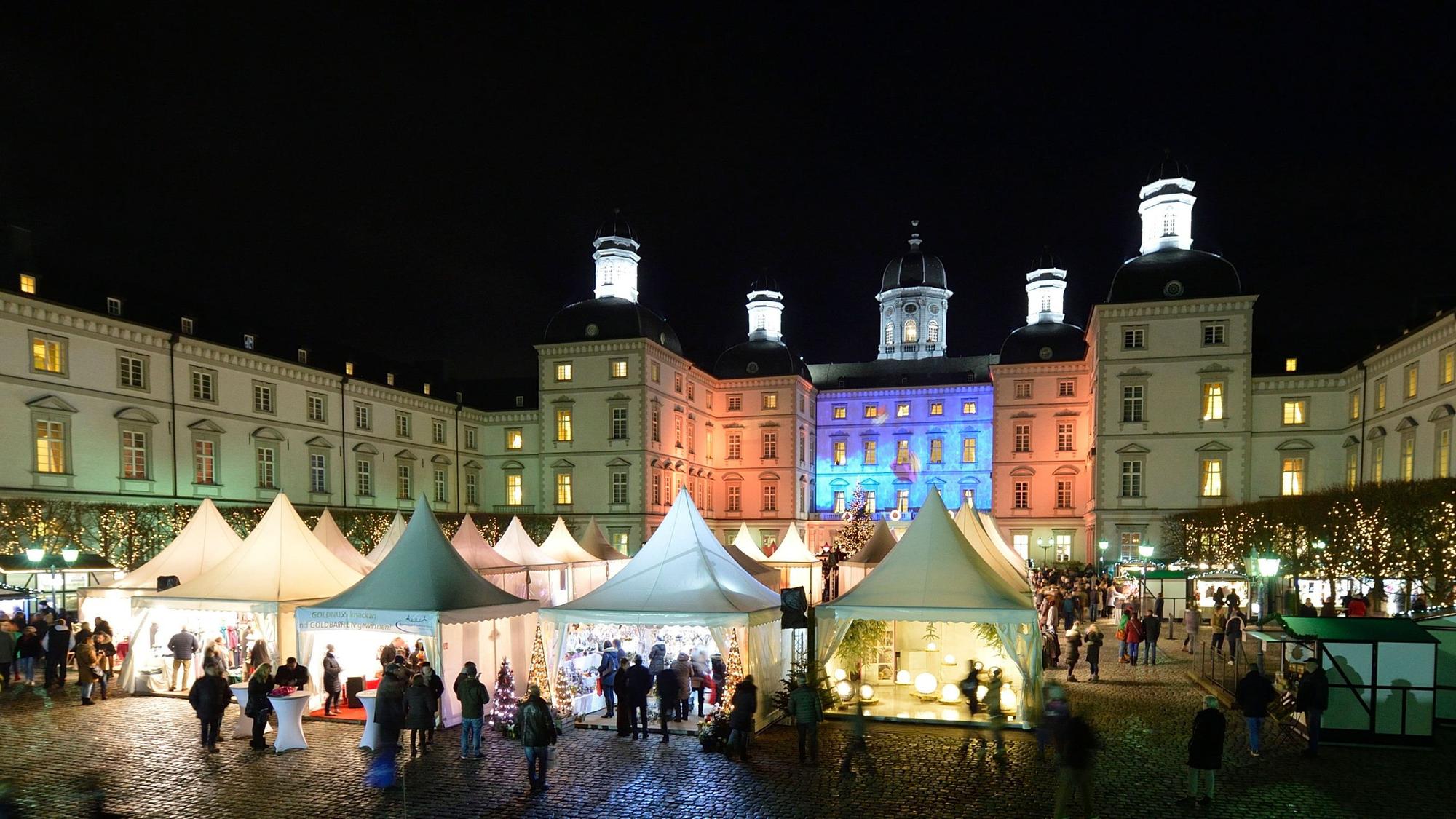 Weihnachtsmarkt vor Schloss Bensberg: Im Schlosshof stehen weiße Pavillon, das Schloss wird im Dunkeln angestrahlt.