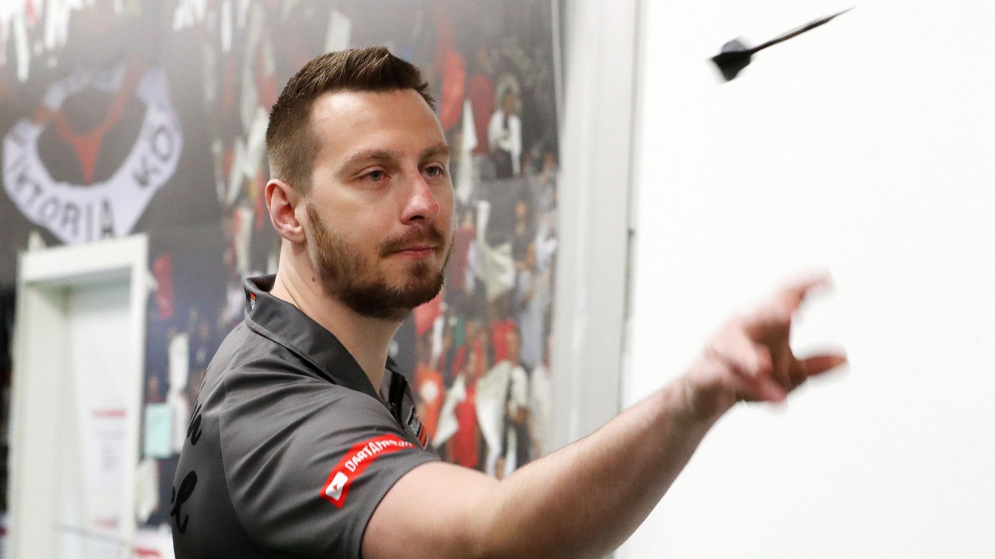Darts-Profi Florian Hempel im Vip-Zelt des FC Viktoria Köln. Er hat gerade einen Dart-Pfeil geworfen. Der Pfeil fliegt vor ihm.