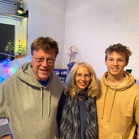 Ein Mann und eine Frau und ein jüngerer Mann, Eltern und Sohn, stehen nebeneinander, im Hintergrund sind mit Lichterketten beleuchtete Lego-Aufbauten zu sehen.