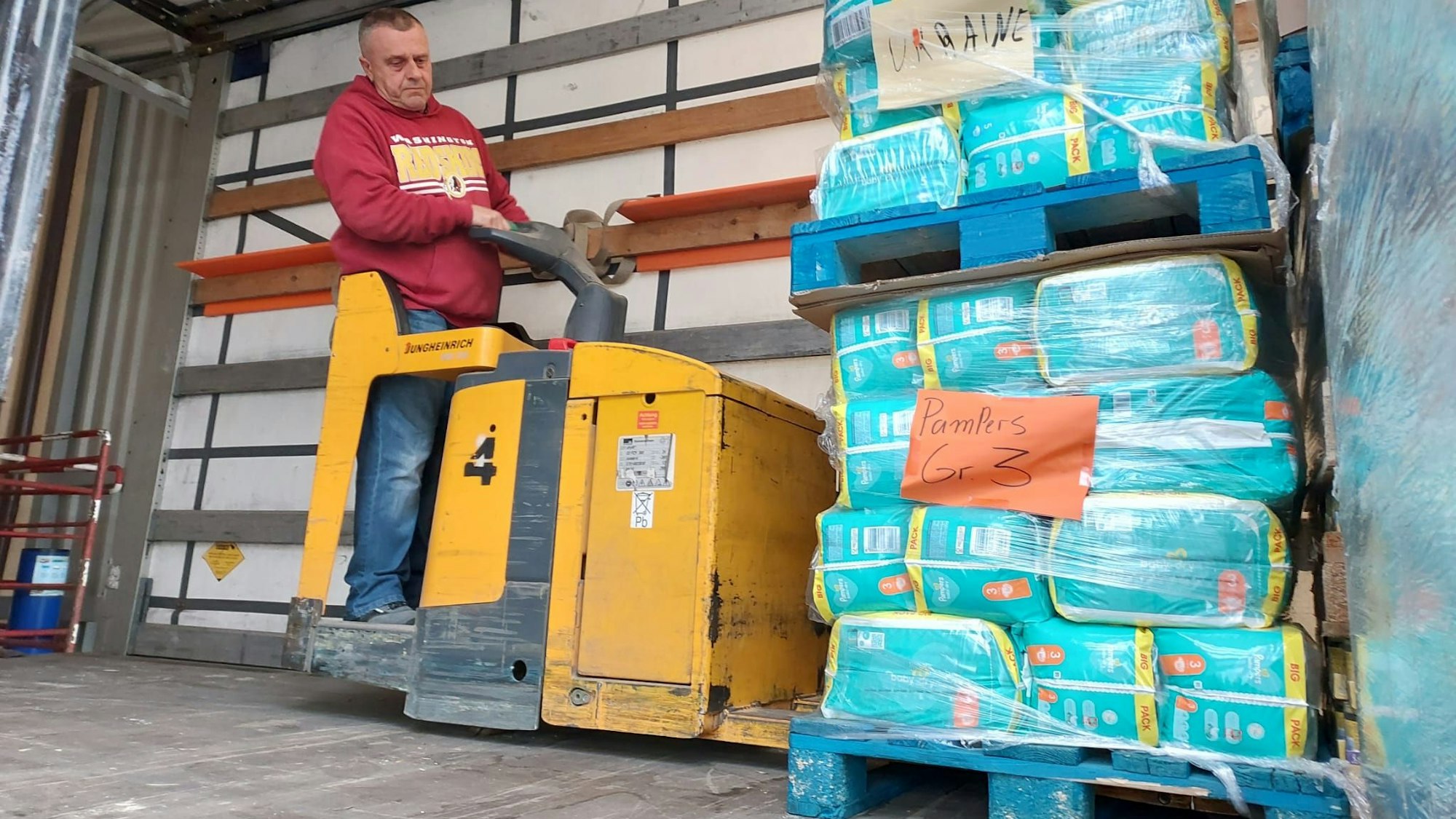 EIn Mann lädt mit einem Stapler zwei Paletten mit Windelpackungen auf einen Lkw.
