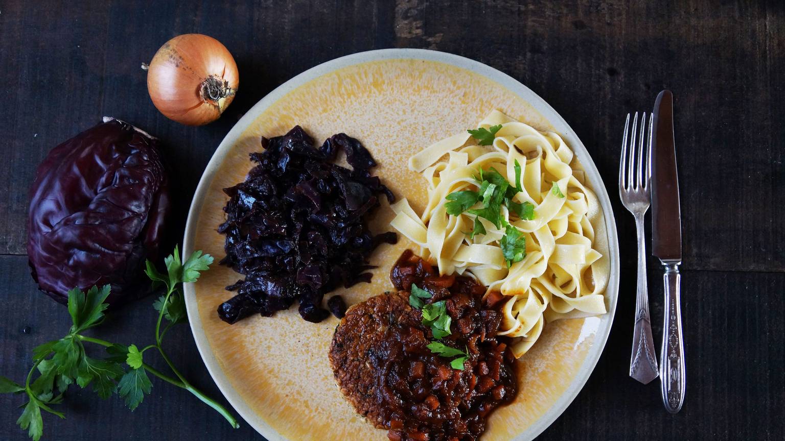 Ein luftiges Tagliatelle-Knäuel bildet mit weihnachtlichem Rotkraut und der krossen Veggie-Frikadelle ein Trio auf dem Teller.