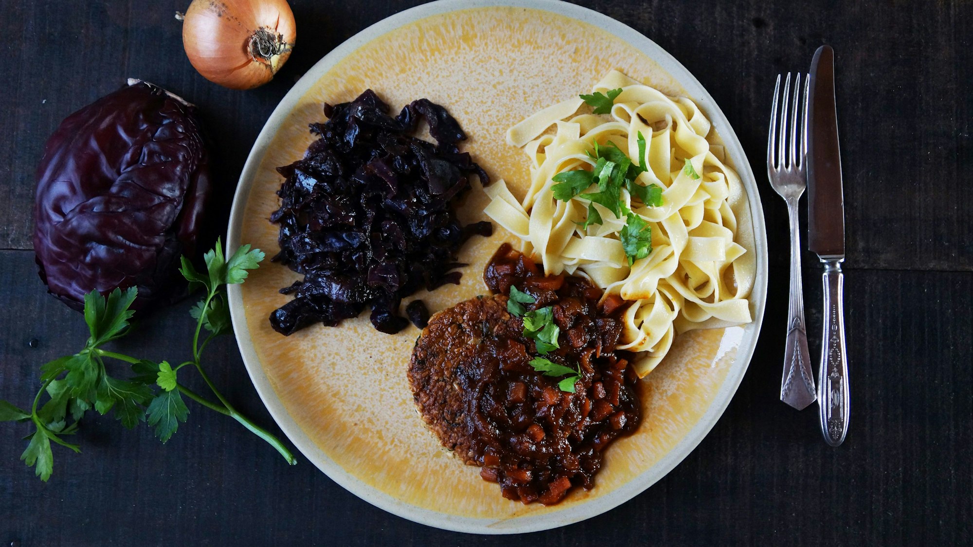 Ein luftiges Tagliatelle-Knäuel bildet mit weihnachtlichem Rotkraut und der krossen Veggie-Frikadelle ein Trio auf dem Teller.