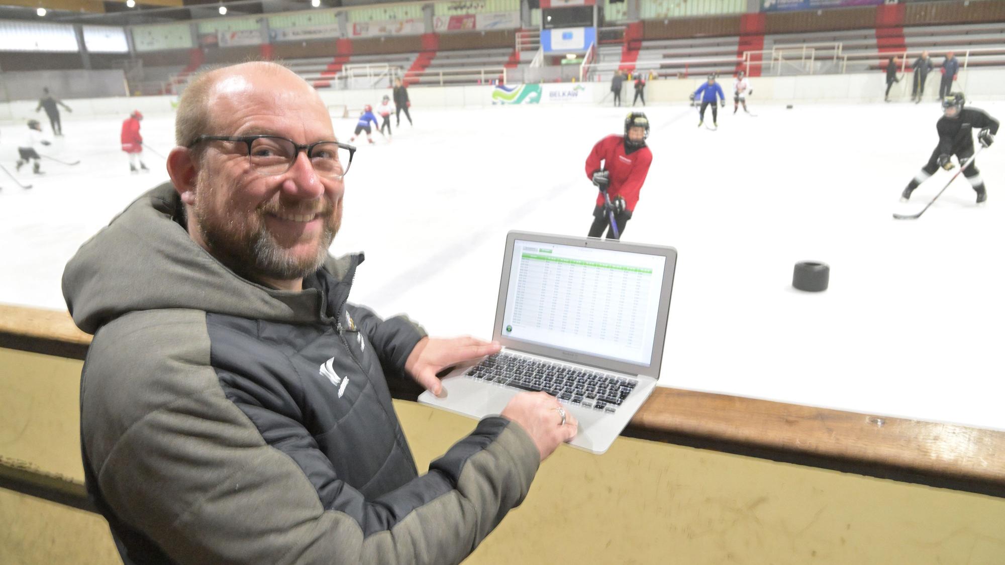 Peter Schüller, Vorstandsmitglied des Eissportvereins Bergisch Gladbach, steht mit Laptop am Rand der Eisbahn, während darauf Jugendliche Eishockey spielen.