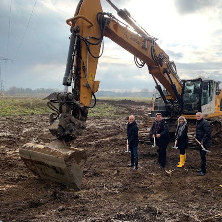 Vor einem Bagger stehen mit Spaten der Technische Beigeordnete der Stadt Troisdorf, Walter Schaaf, Bürgermeister Alexander Biber sowie die Geschäftführung der TroiKomm Andrea Vogt und Michael Roelofs.