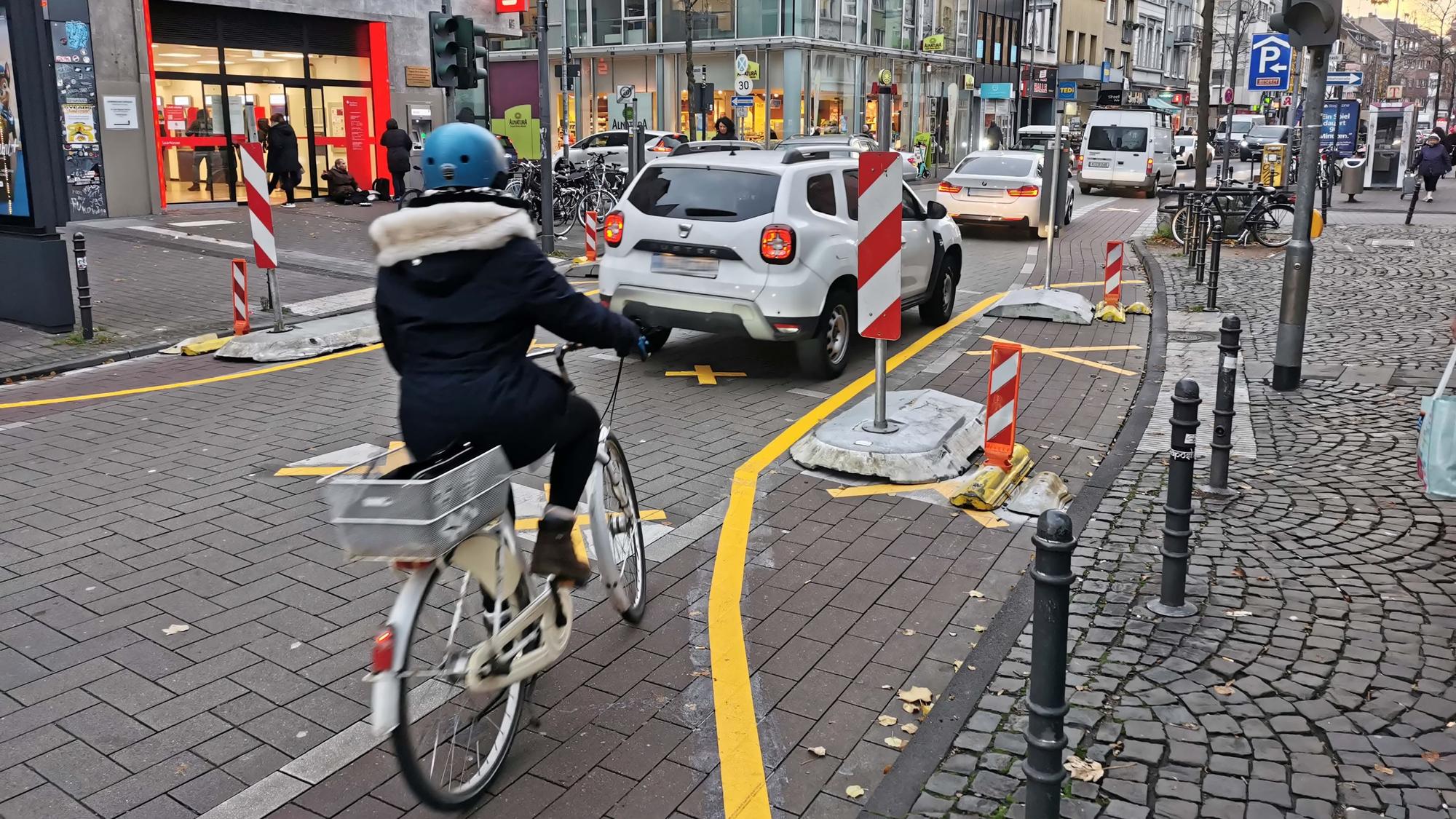 Eine Radfahrerin fährt auf der Venloer Straße hinter mehreren Autos durch eine Engstelle.
