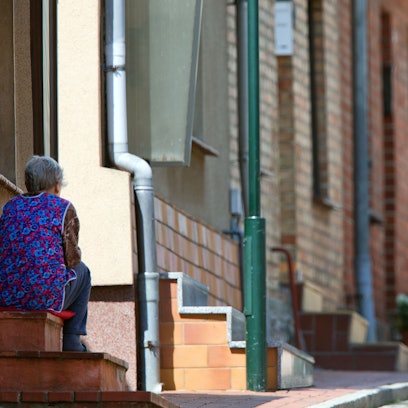 Ein ältere Frau sitzt auf der Treppe vor ihrem Wohnhaus.