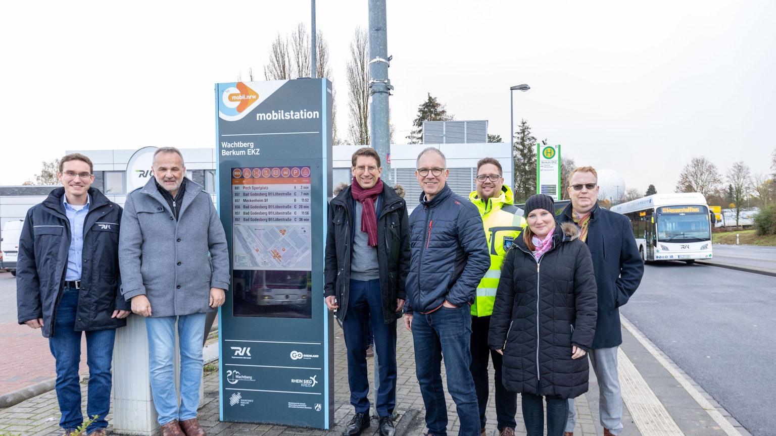 Sechs Männer und eine Frau stehen an der neuen Mobilstation in Berkum, einem Gehäuse, in dem ein hochformatiger Bildschirm steckt.