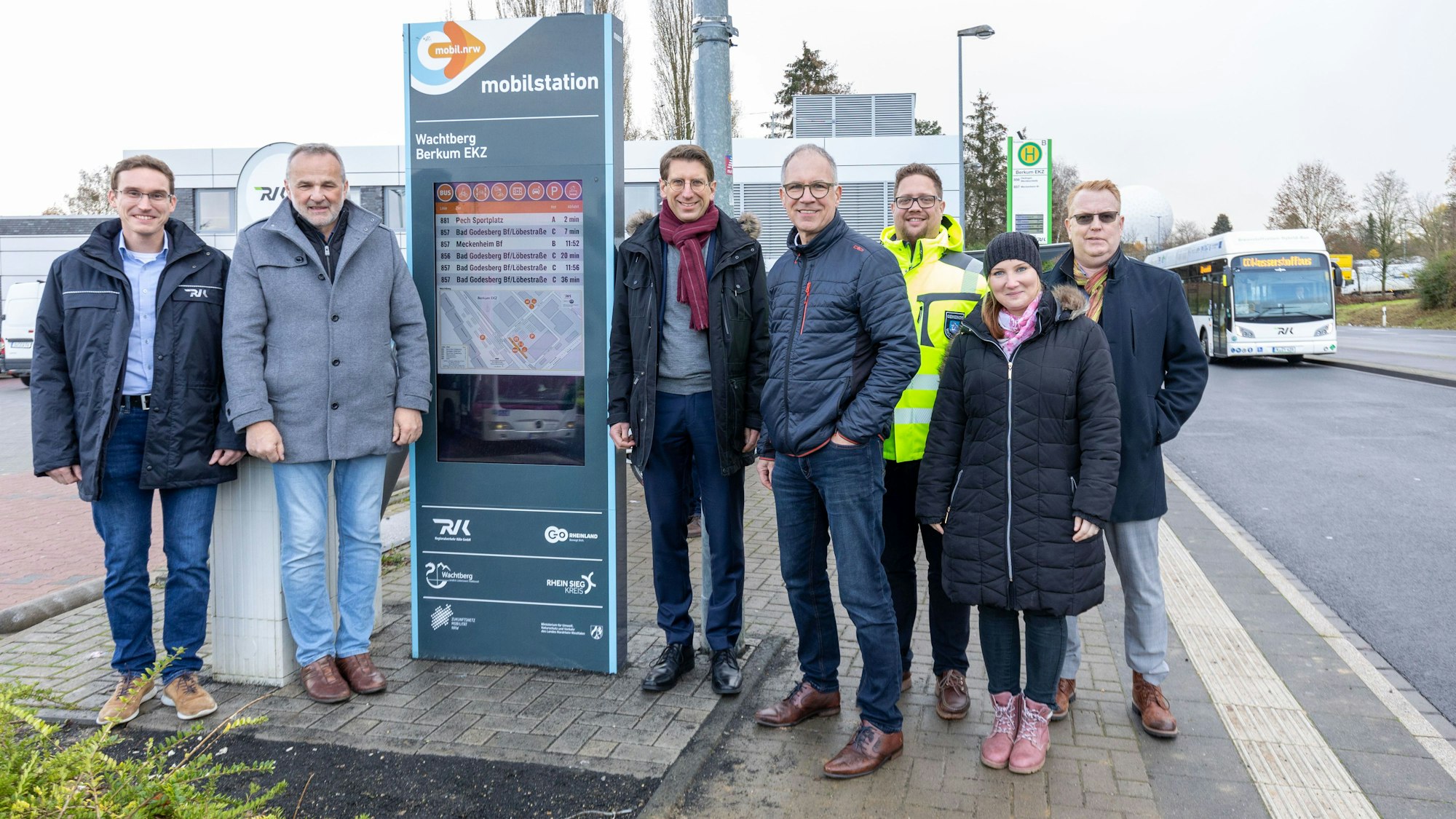 Sechs Männer und eine Frau stehen an der neuen Mobilstation in Berkum, einem Gehäuse, in dem ein hochformatiger Bildschirm steckt.