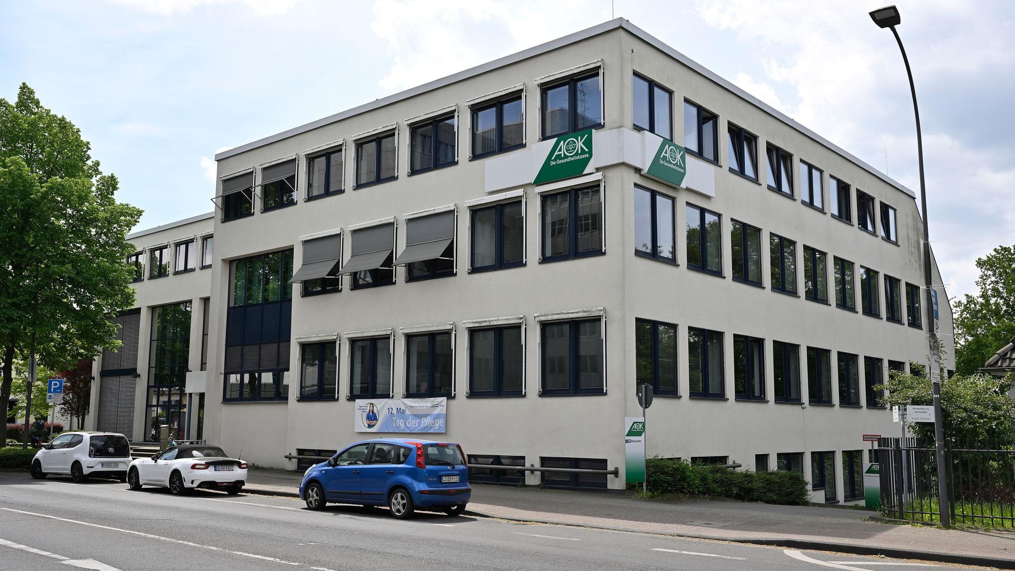 Das dreigeschossige AOK-Gebäude mit drei Autos davor an der Bensberger Straße.