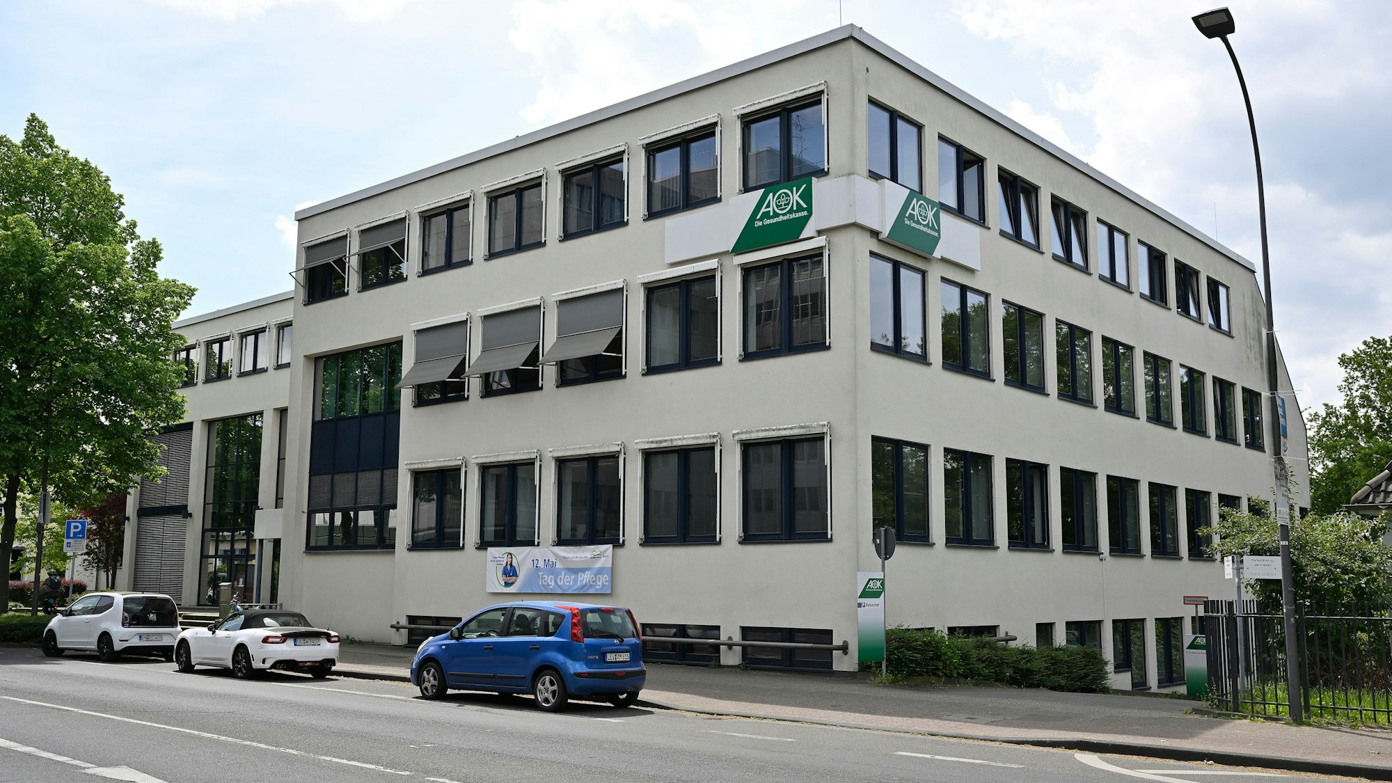 Das dreigeschossige AOK-Gebäude mit drei Autos davor an der Bensberger Straße.