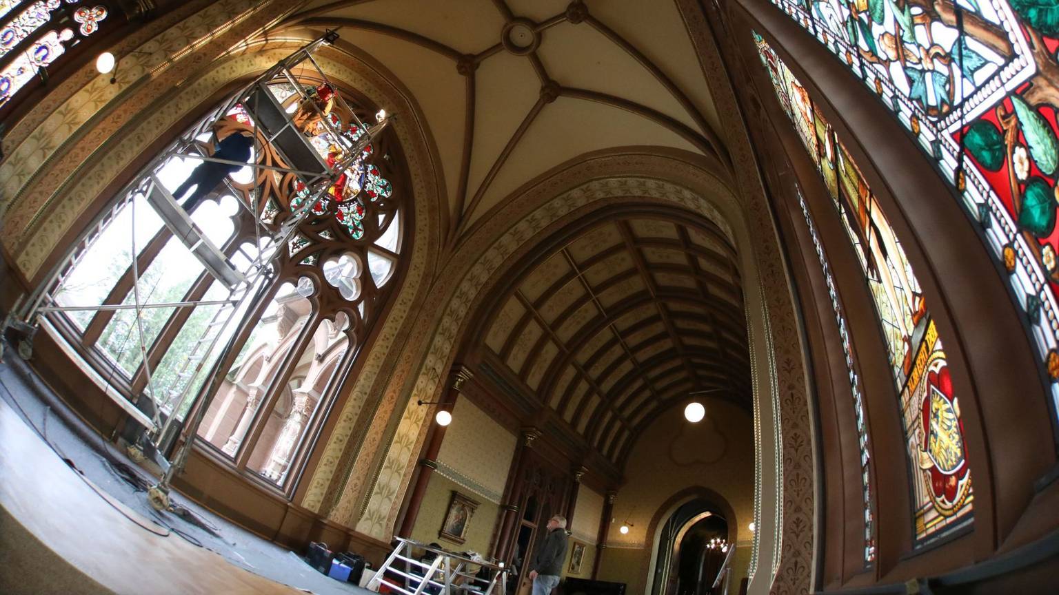 In der großen und hohen Kunsthalle von Schloss Drachenburg sind rechts die schon rekonstruierten Buntglasscheiben zu sehen. Auf der linken Seite setzen die Experten von einem Gerüst aus die letzten Scheiben ein.