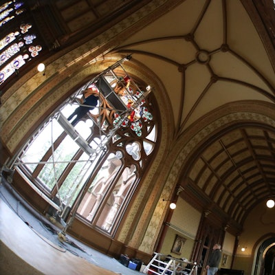 In der großen und hohen Kunsthalle von Schloss Drachenburg sind rechts die schon rekonstruierten Buntglasscheiben zu sehen. Auf der linken Seite setzen die Experten von einem Gerüst aus die letzten Scheiben ein.