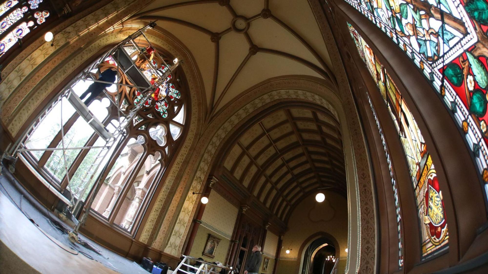 In der großen und hohen Kunsthalle von Schloss Drachenburg sind rechts die schon rekonstruierten Buntglasscheiben zu sehen. Auf der linken Seite setzen die Experten von einem Gerüst aus die letzten Scheiben ein.