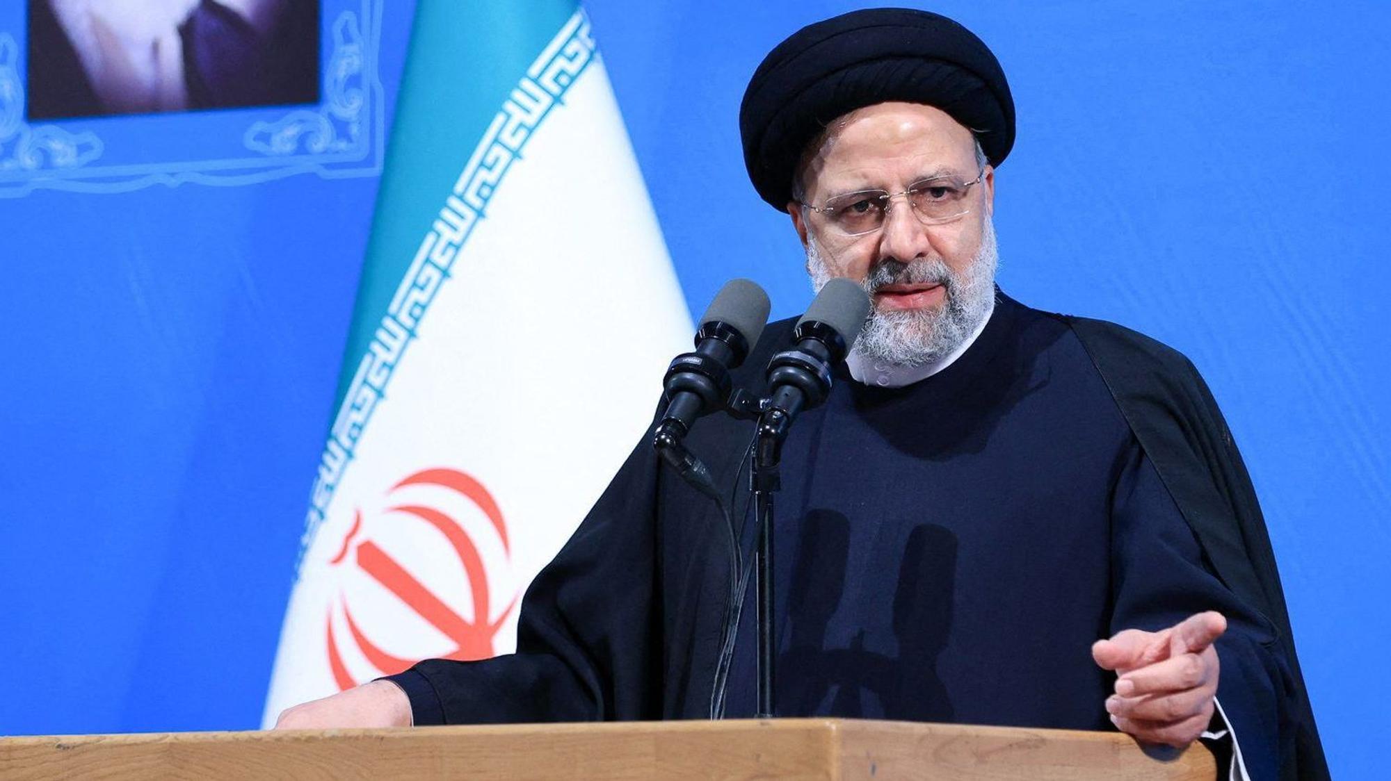 Der iranische Präsident Ebrahim Raisi steht an einem Pult und spricht in Mikrofone.
