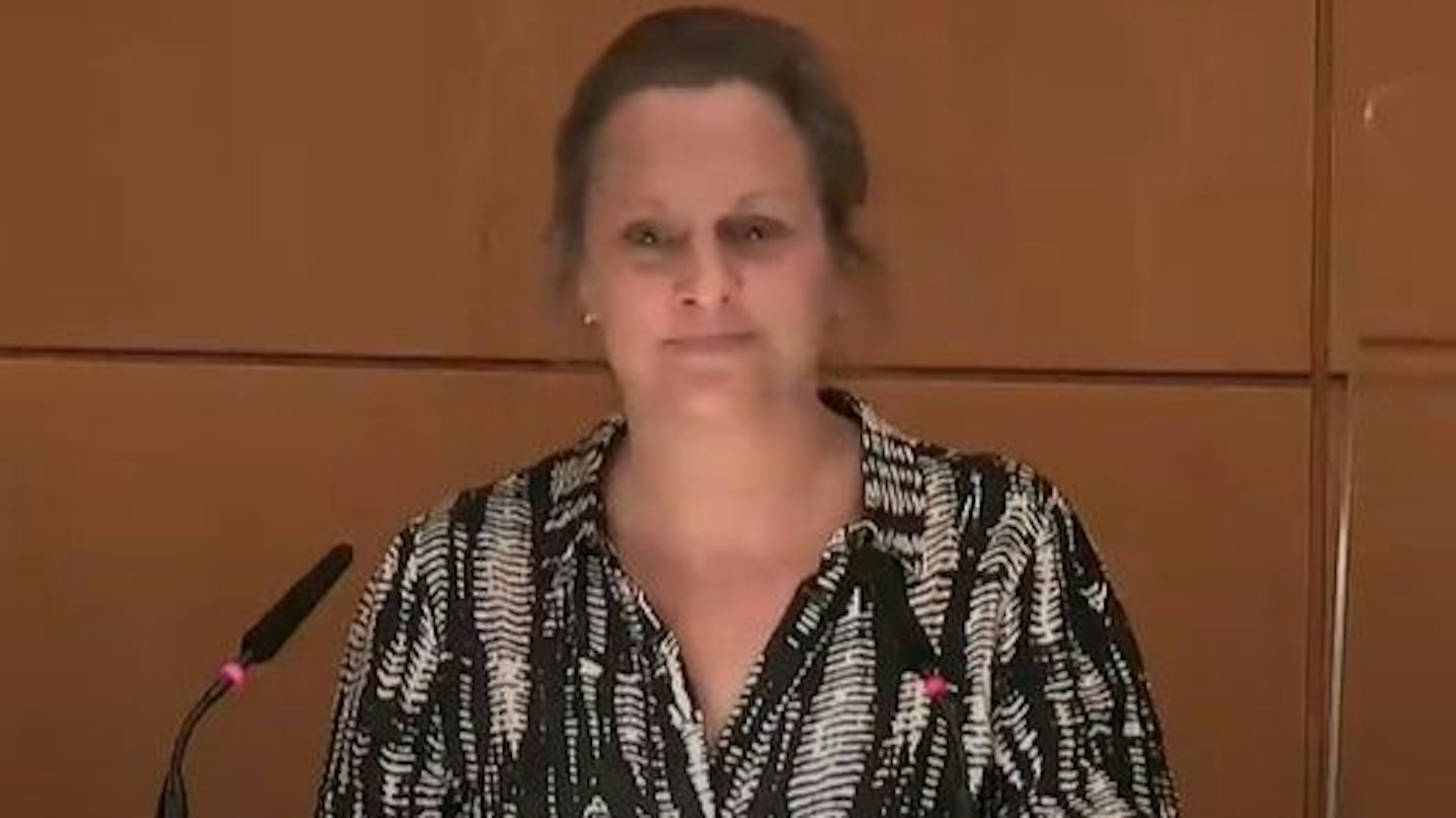 In dieser Szene klebt sich Ratsmitglied Nicole Gabrysch (Klimafreunde) mit ihrer linken Hand am Rednerpult des Ratssaals fest.