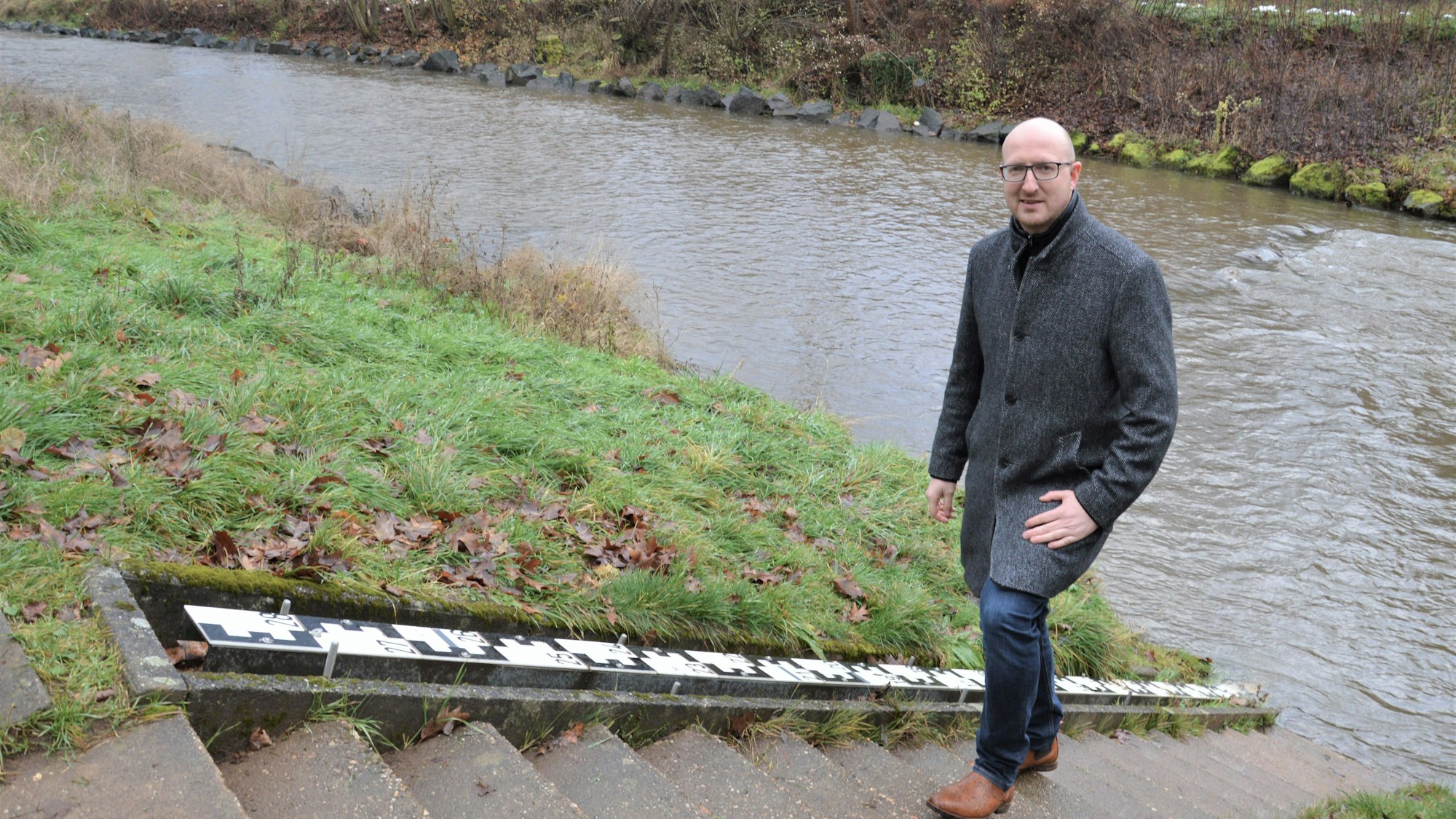 Bürgermeister Ingo Pfennigs steht auf einer Treppe am Messpegel der Urft in Gemünd.