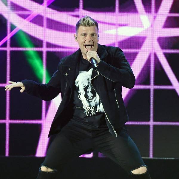 Backstreet-Boys-Sänger Nick Carter hält ein Mikrofon in der Hand und singt auf einer Bühne vor pinkem-schwarzem Hintergrund.