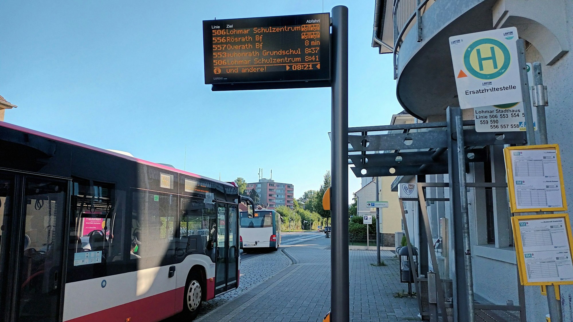 Ein Bus hält an einer Haltestelle. Eine elektronische Anzeige zeigt die Abfahrtezeiten an.