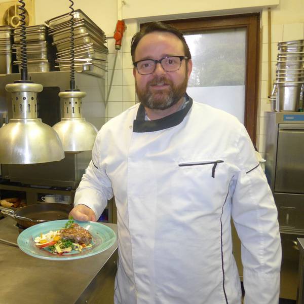 Johannes Richter steht in der Restaurant-Küche und posiert mit einem angerichteten Teller für die Kamera.
