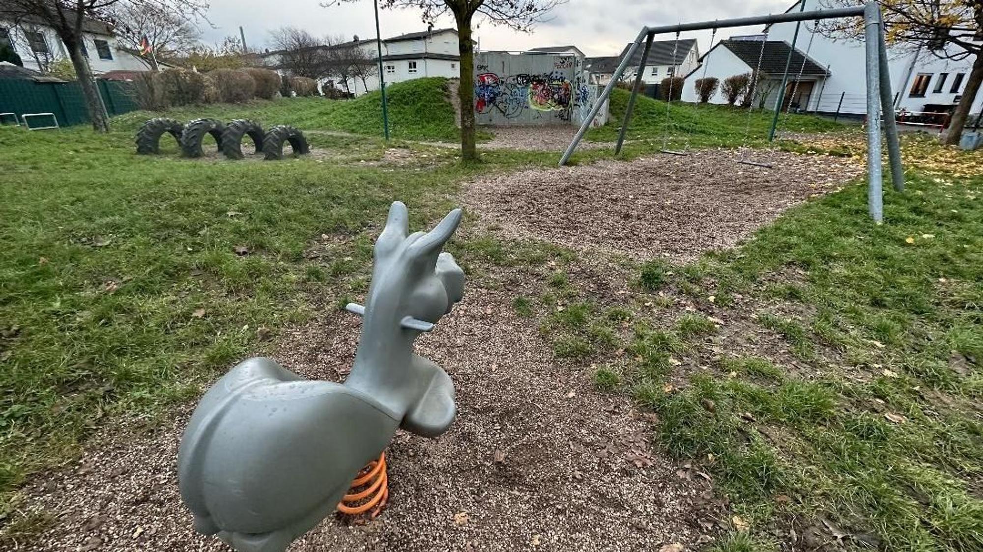 Ein leerer Spielplatz in Niederkassel. Im Vordergrund ist eine Wippe für eine Person, die die Form eines Esels hat. Im Hintergrund sind Schaukeln und Reifen.