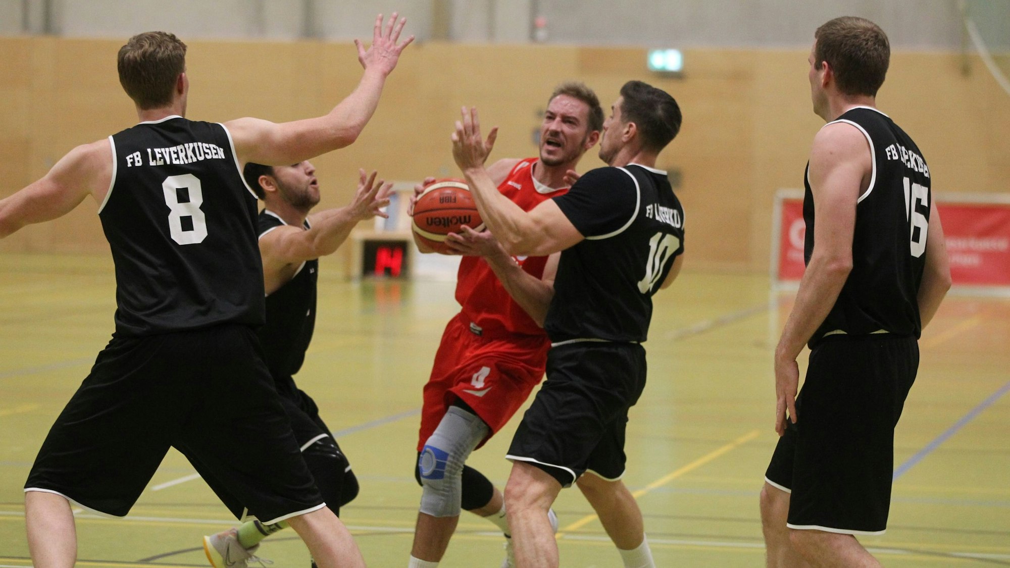 Bad Münstereifels Spieler Jan Winkelnkemper im roten Trikot ist umringt von vier Leverkusener Gegenspielern in schwarzen Trikots.