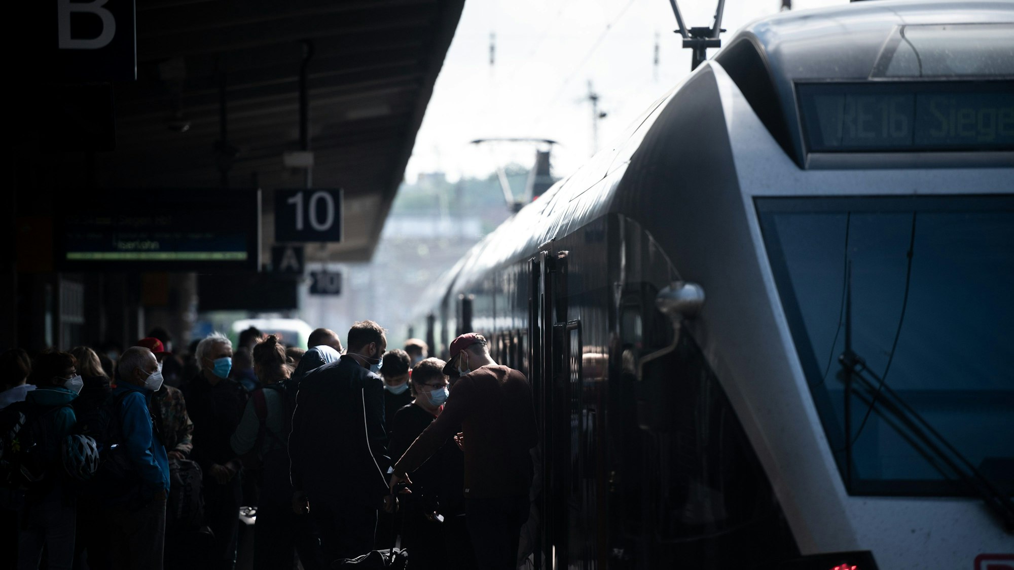 Zu sehen ist ein Zug, der an einem Bahnsteig steht, Menschen drängeln sich beim ein- und aussteigen.