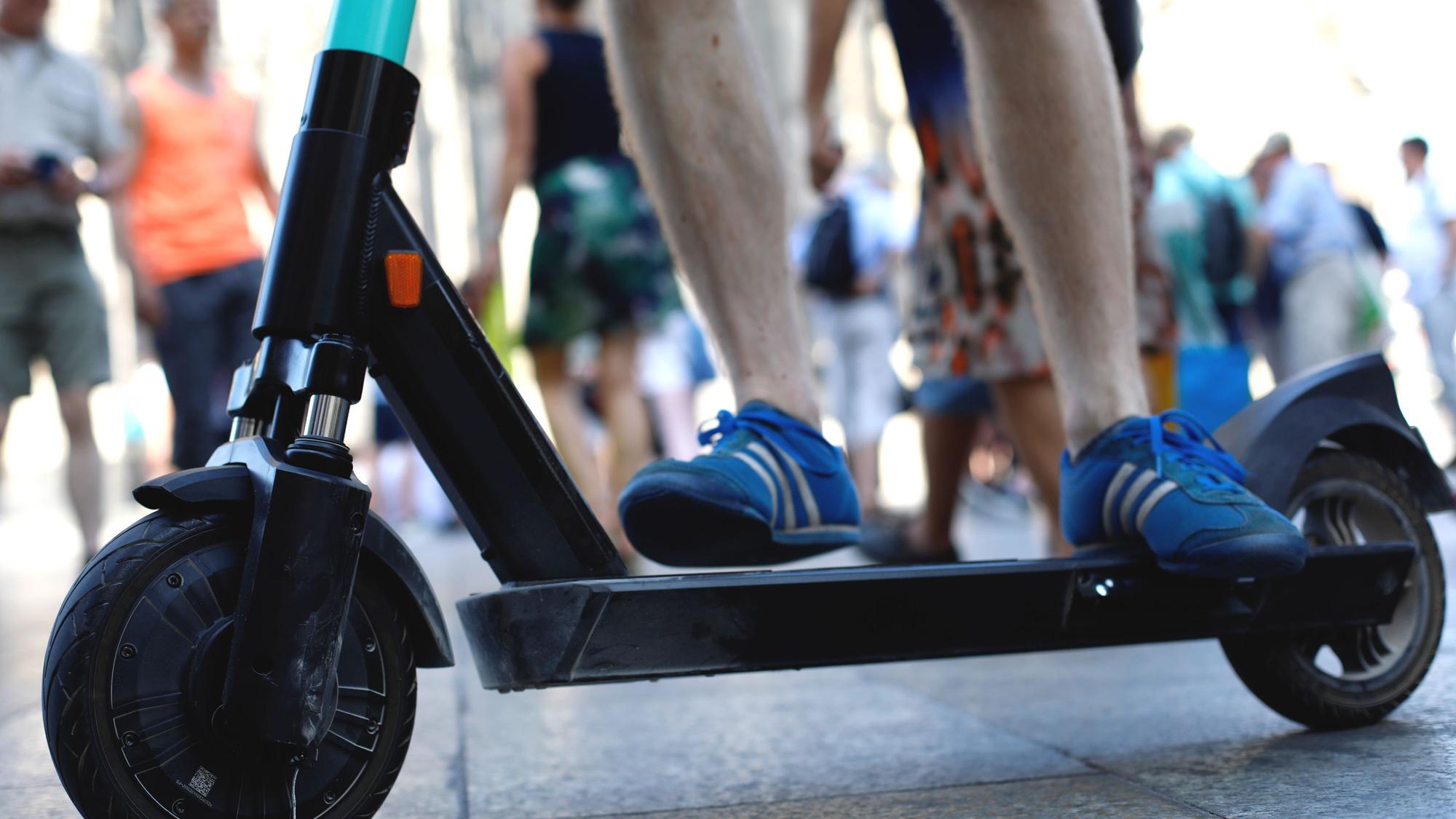 Ein E-Scooter ist zwischen Fußgängern unterwegs.