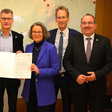 Ministerin Ina Scharrenbach überreicht Bürgermeister Jan Lembach im Schmidtheimer Rathaus den 13-Millionen-Euro Förderbescheid. Gemeinsam mit Erwin Bungartz, Melissa Brandt, Detlef Seif und Ralf Nolten posieren sie für ein Foto.