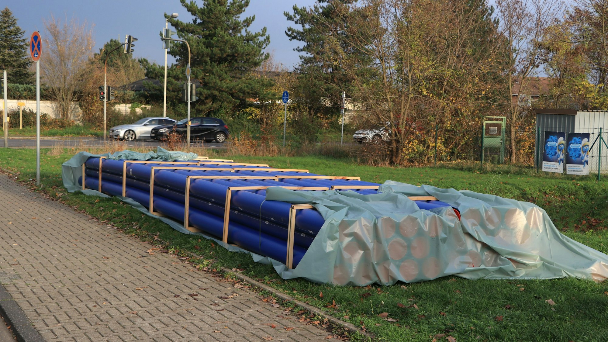 Die neuen blauen Abwasserrohre liegen bereits auf einer Wiese neben der Straße bereit.