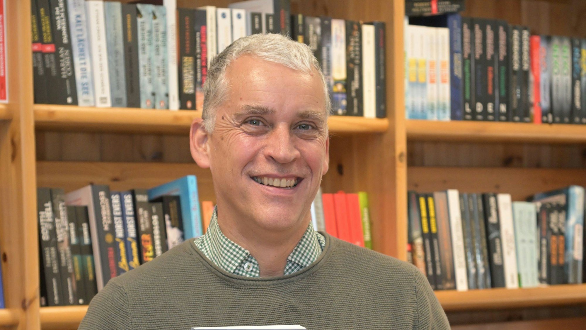 Alexander Bücken steht vor einem Holzbücherregal.