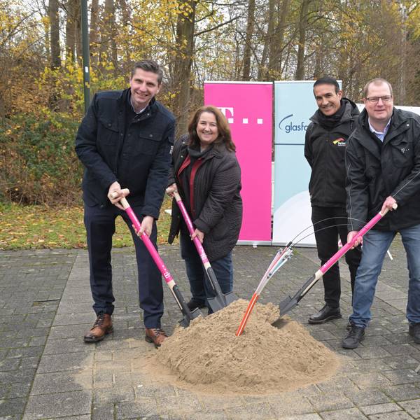 Vier Männer und Bondina Schulze, Bürgermeisterin von Rösrath, stoßen symbolisch einen Spaten in ein Sandhäufchen, aus dem Glasfasern ragen.