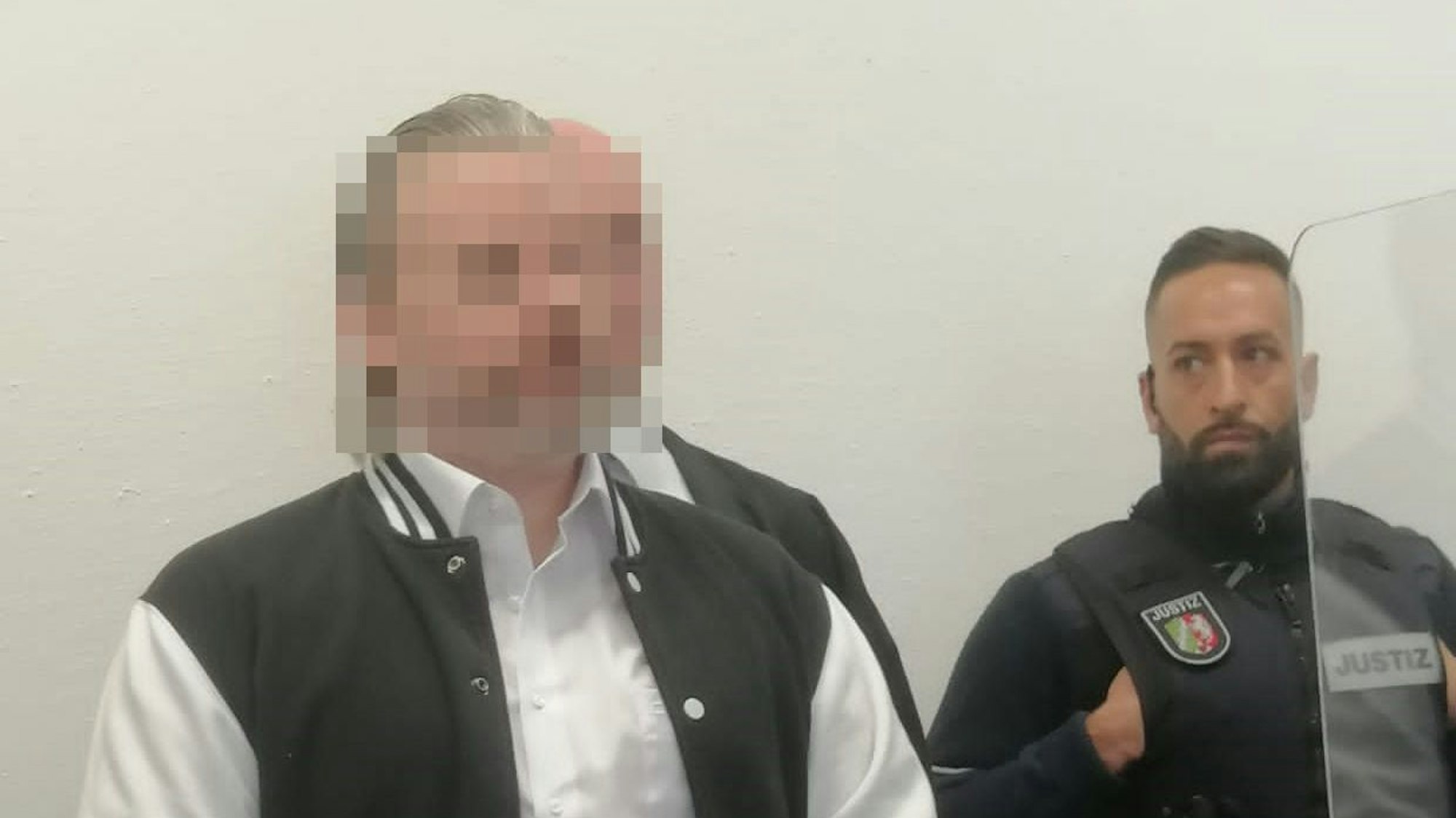 Das Bild zeigt den Angeklagten an der Seite eines Wachmanns im Gerichtssaal.