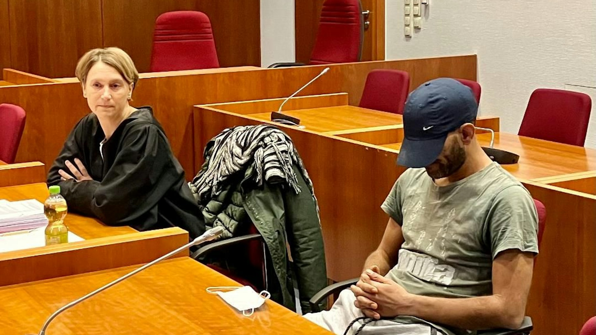 Ein Angeklagter sitzt neben seiner Verteidigerin im Gerichtssaal. Er trägt eine Baseballmütze tief ins Gesicht gezogen.