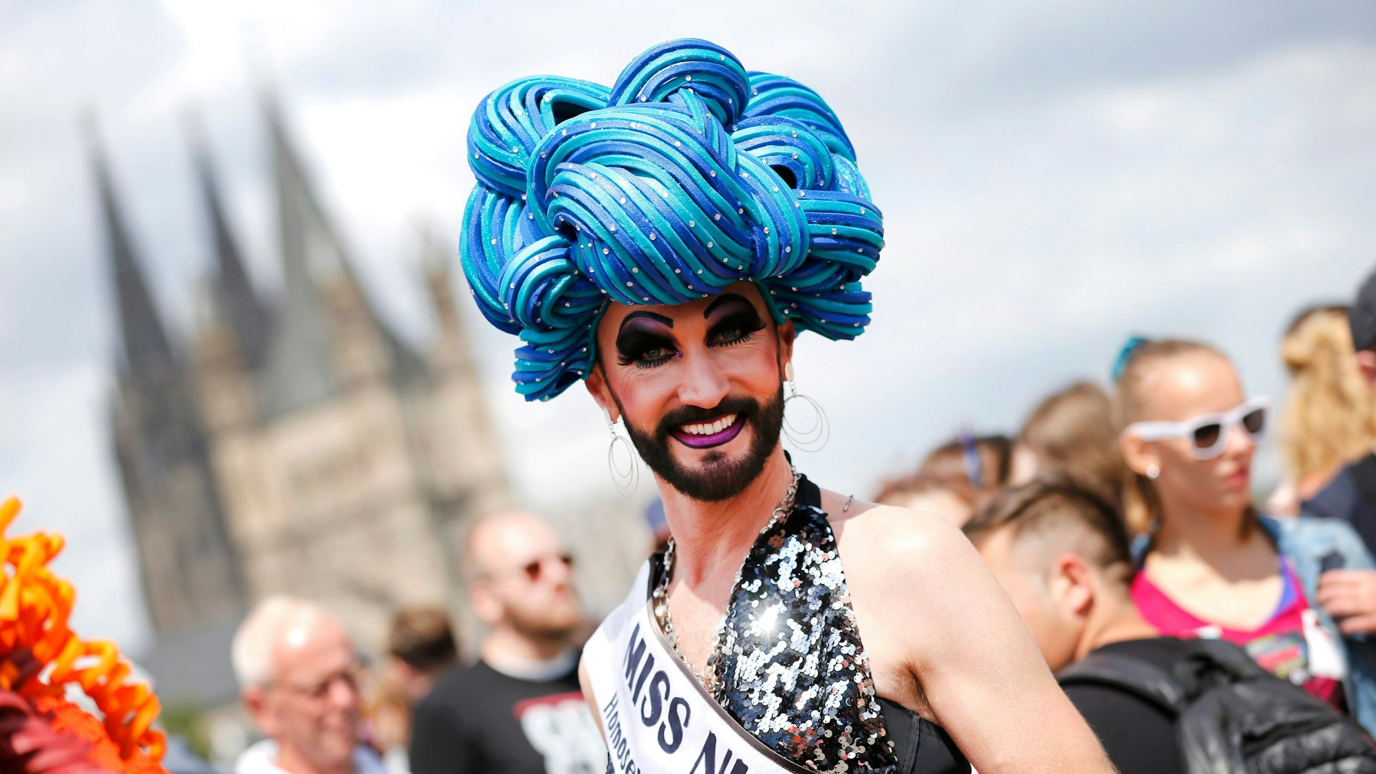 Eine Person mit blauer Perücke steht beim Chistopher Street Day 2019 lächelnd vor der Kamera.