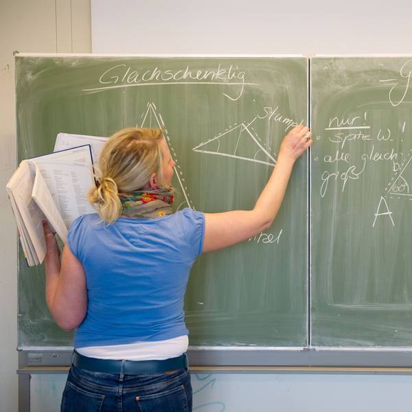 Eine Lehrerin schreibt mit Kreide an die Tafel.
