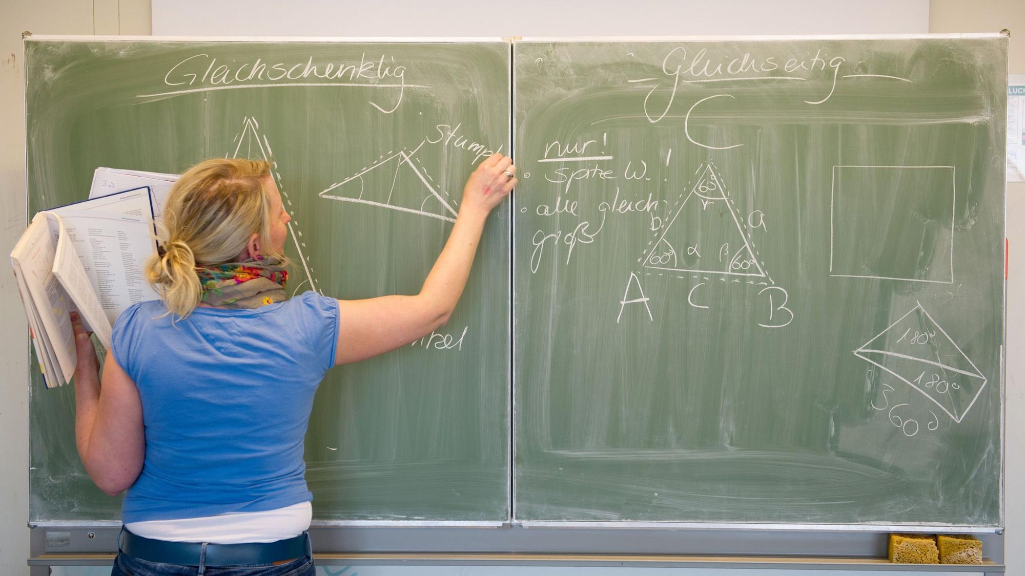 Eine Lehrerin schreibt mit Kreide an die Tafel.