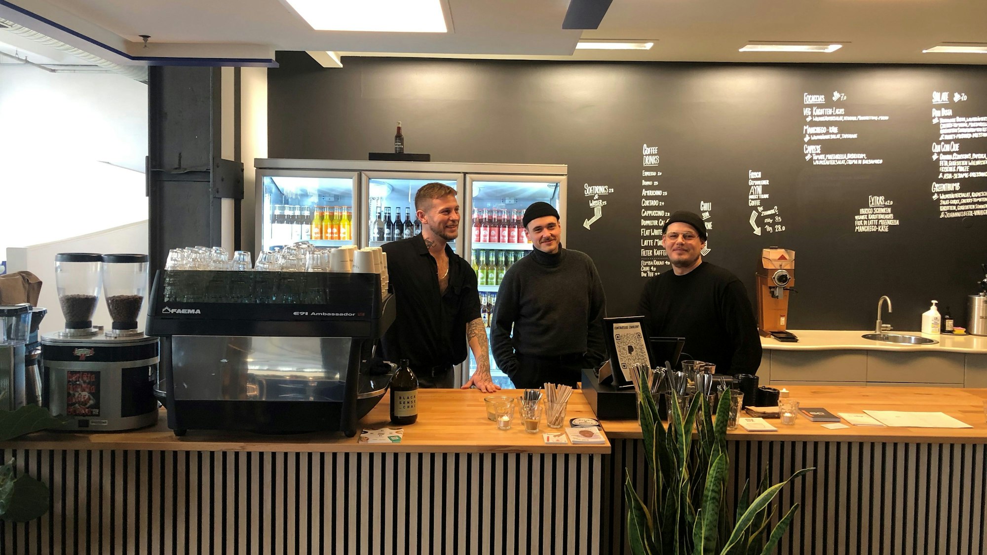 Die drei Betreiber des „Ayni x Schanze“ stehen in schwarzen Pullovern hinter der Theke ihres Cafés.