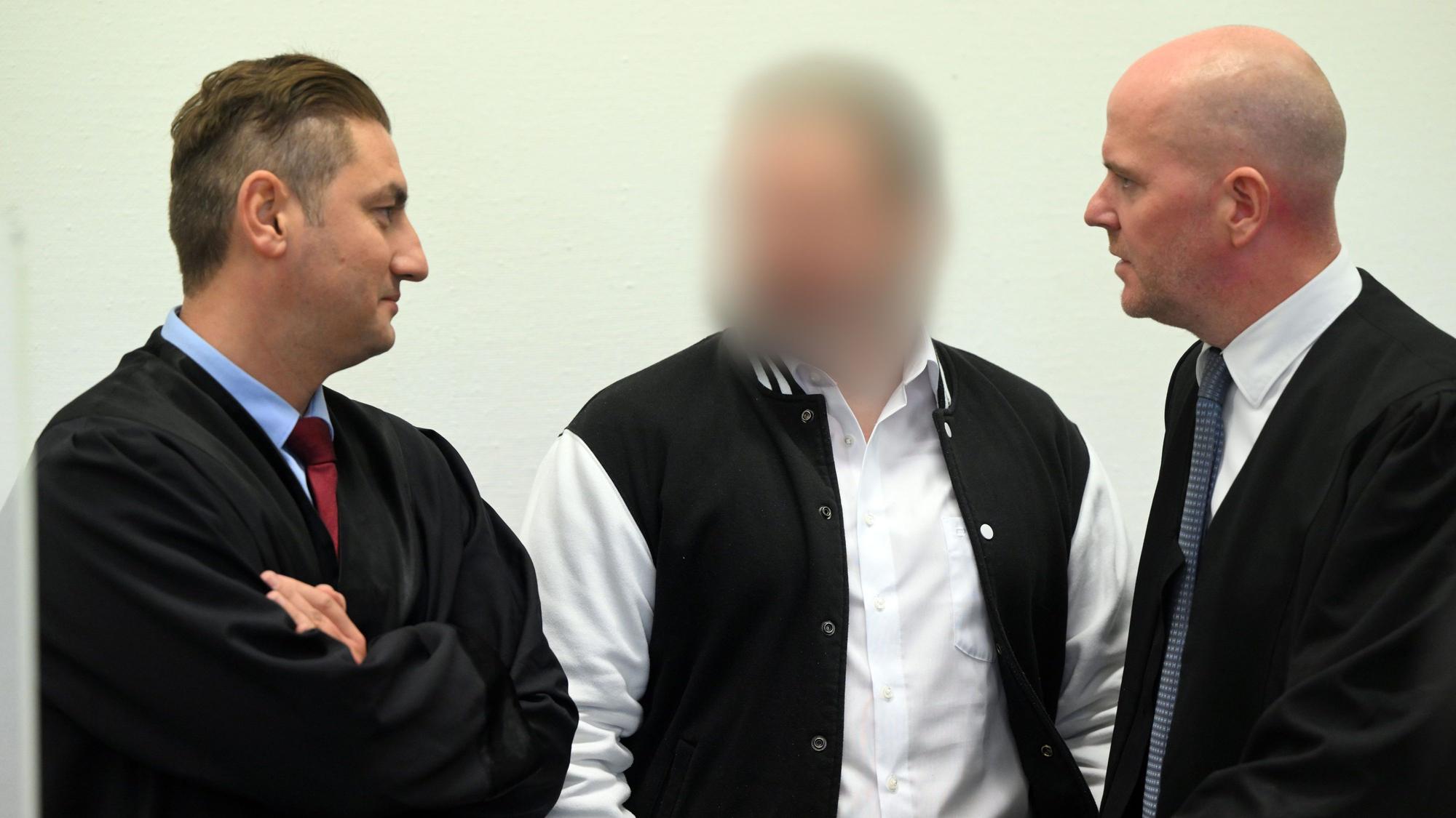Der Angeklagte steht zwischen seinen Anwälten im Kölner Landgericht.